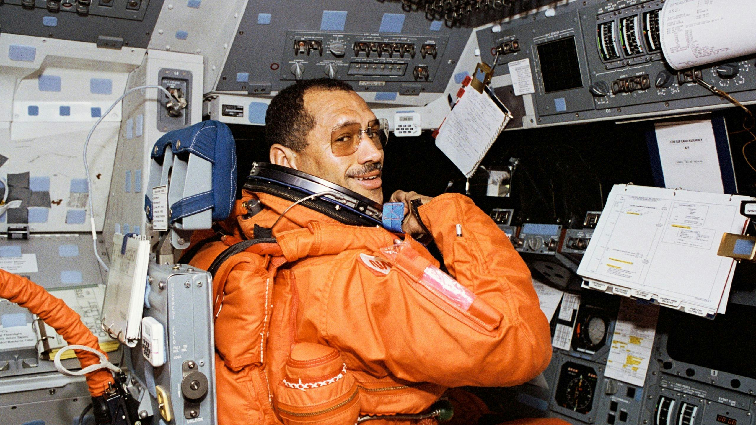 STS-60 commander Charles F Bolden Jr, in his orange launch and entry spacesuit (LES), sits at his st