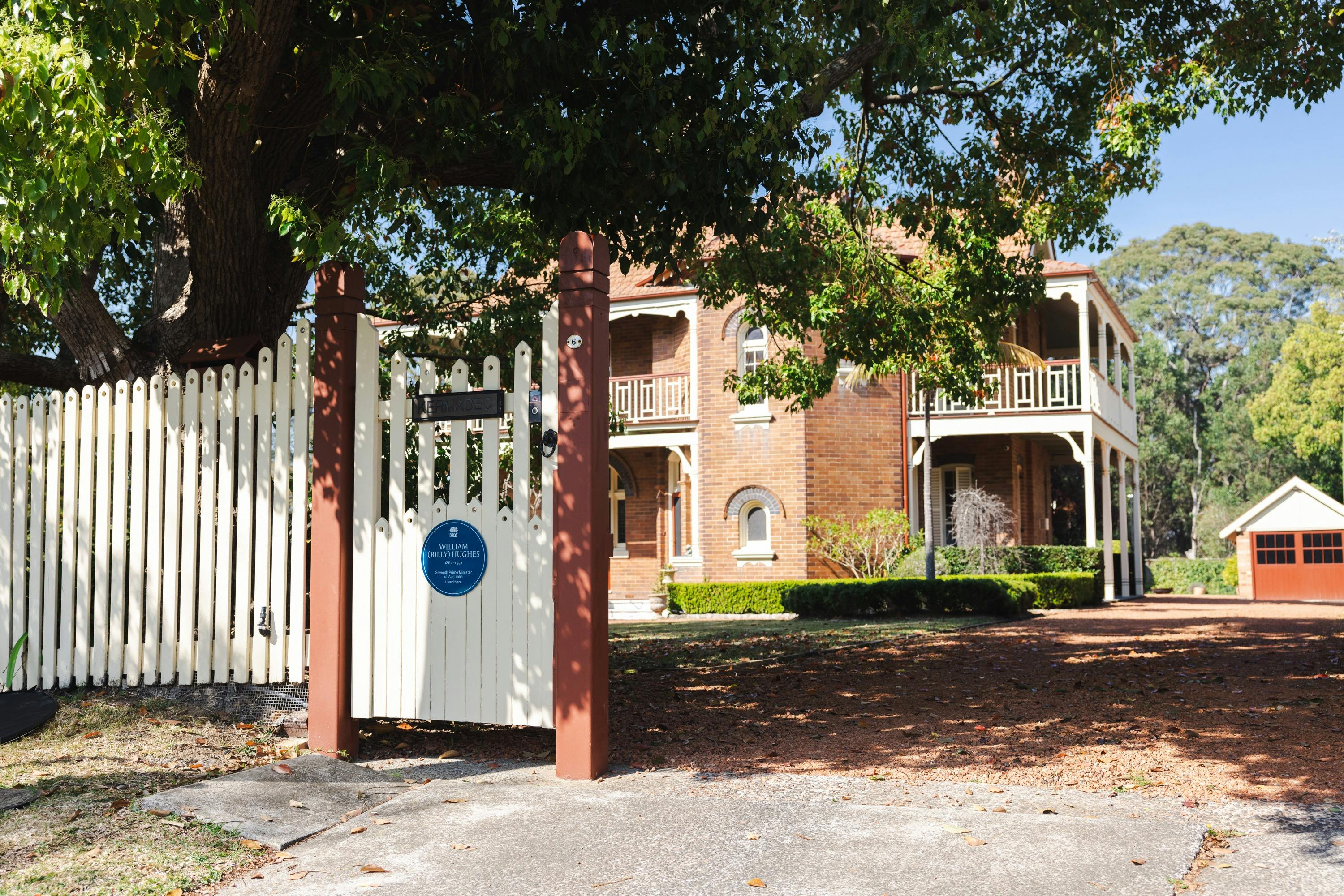 Blue plaque on front fence with two-storey Federation brick home in background