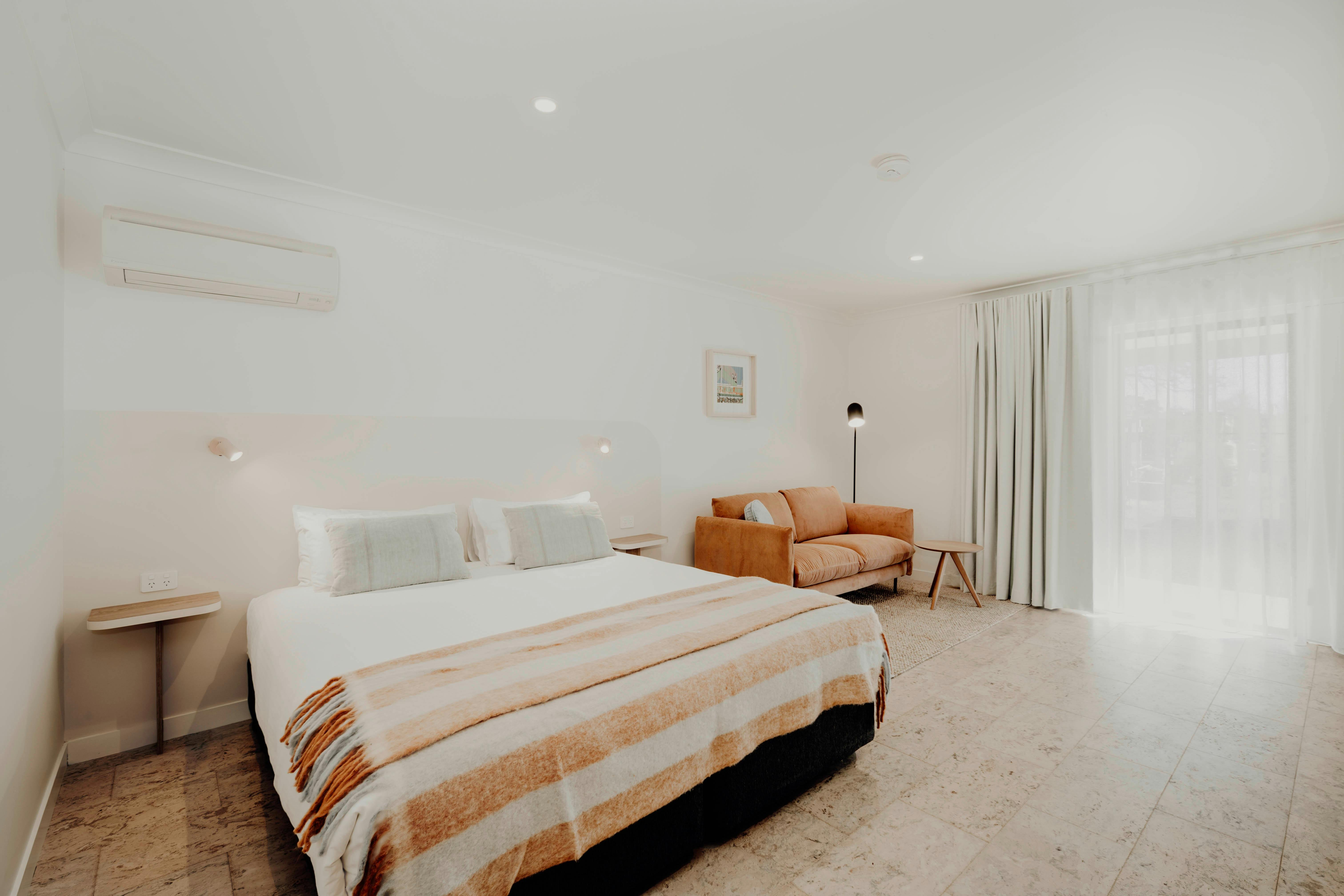 Motel room with king bed and sofa. Crisp white sheets on the bed. Corduroy sofa and lamp.