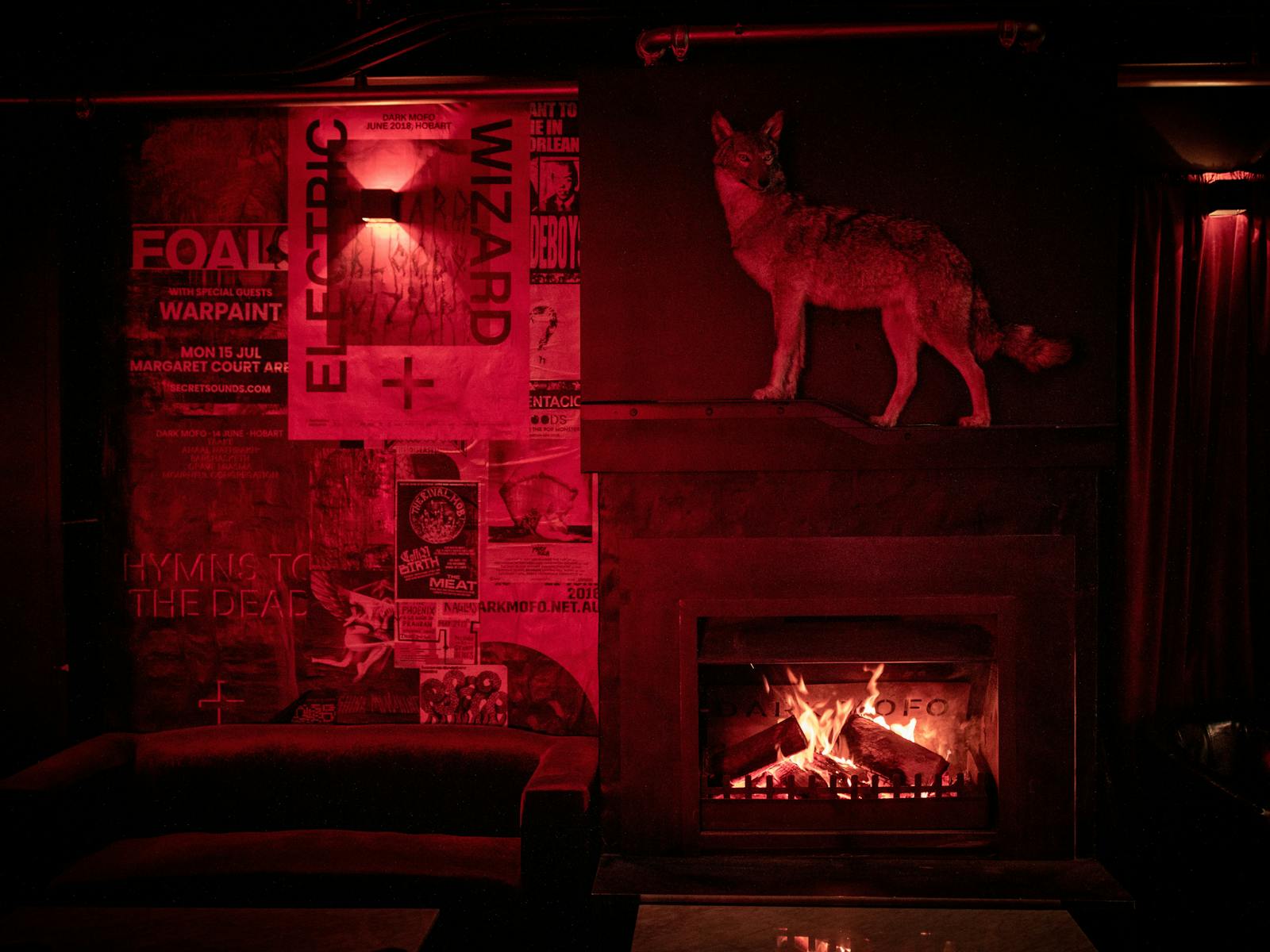 A taxidermy coyote stands on a shelf above a roaring fireplace in the red-lit Altar lounge bar