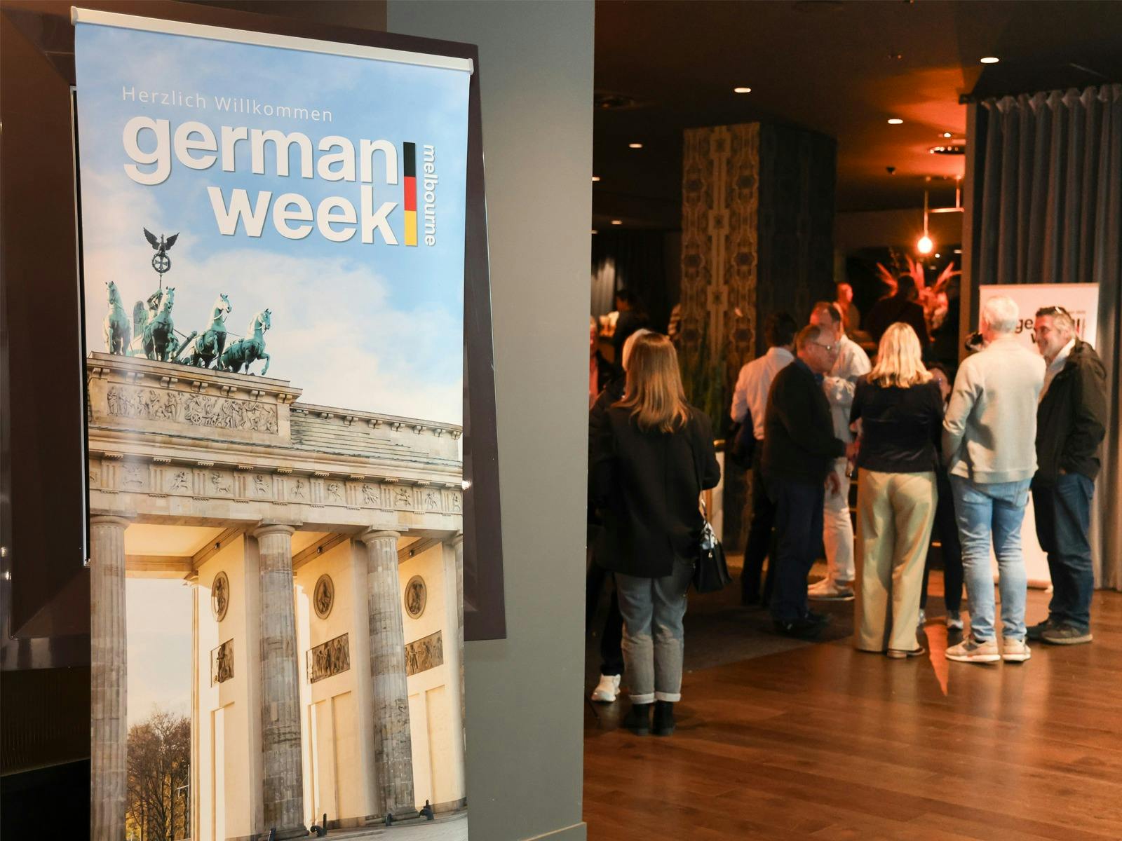 Guests gathering at a German Week Melbourne event beside a banner featuring the Brandenburg Gate.