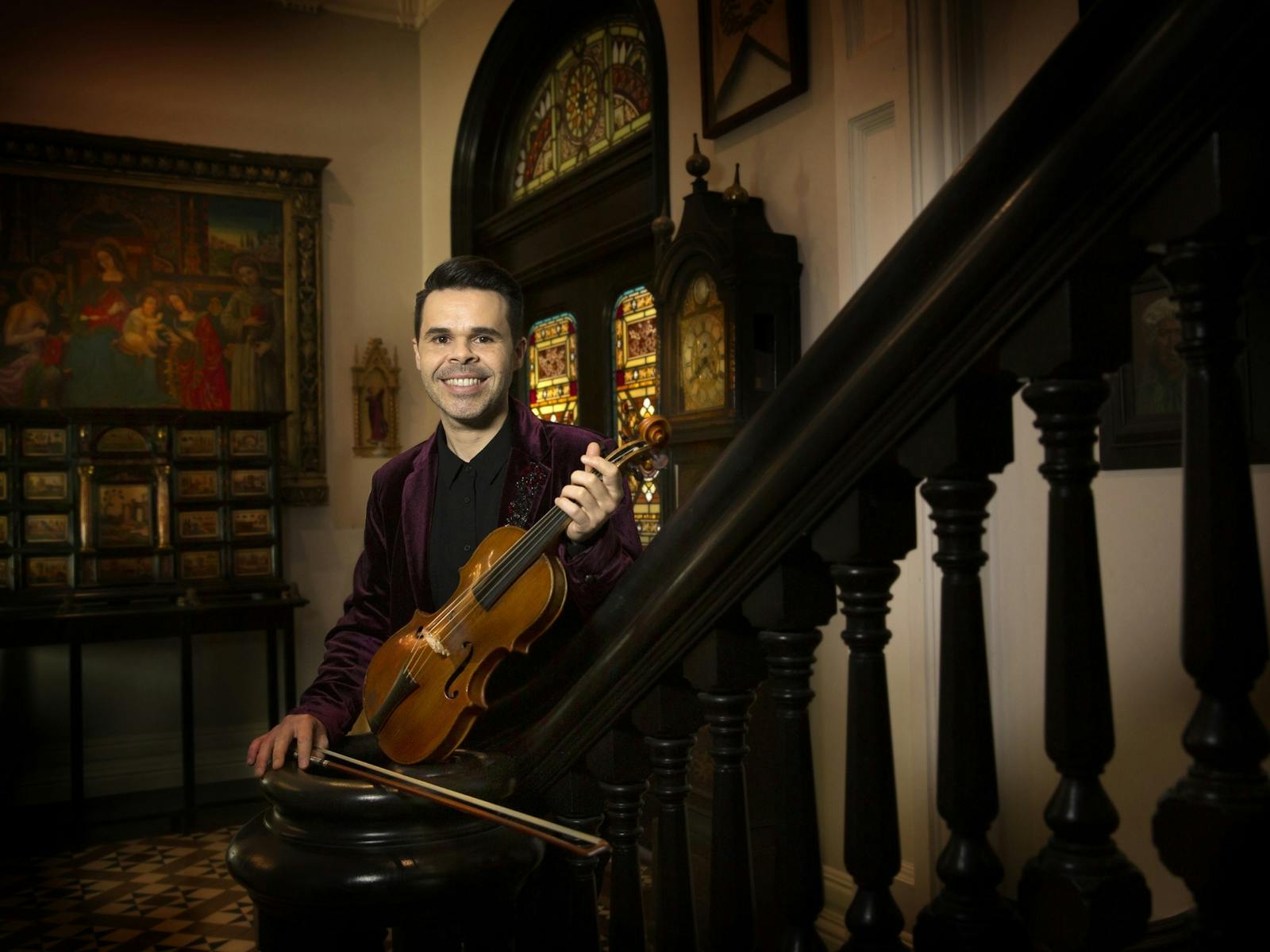 A violinist on a staircase in a grand old house.