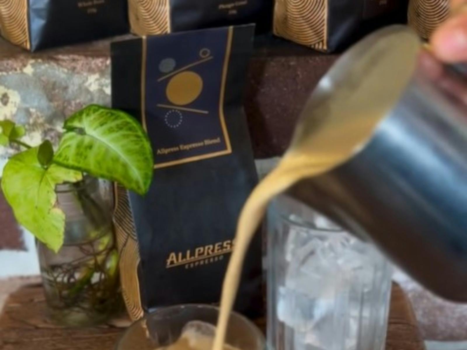 someon pouring coffee over ice with allpress coffee bags in background