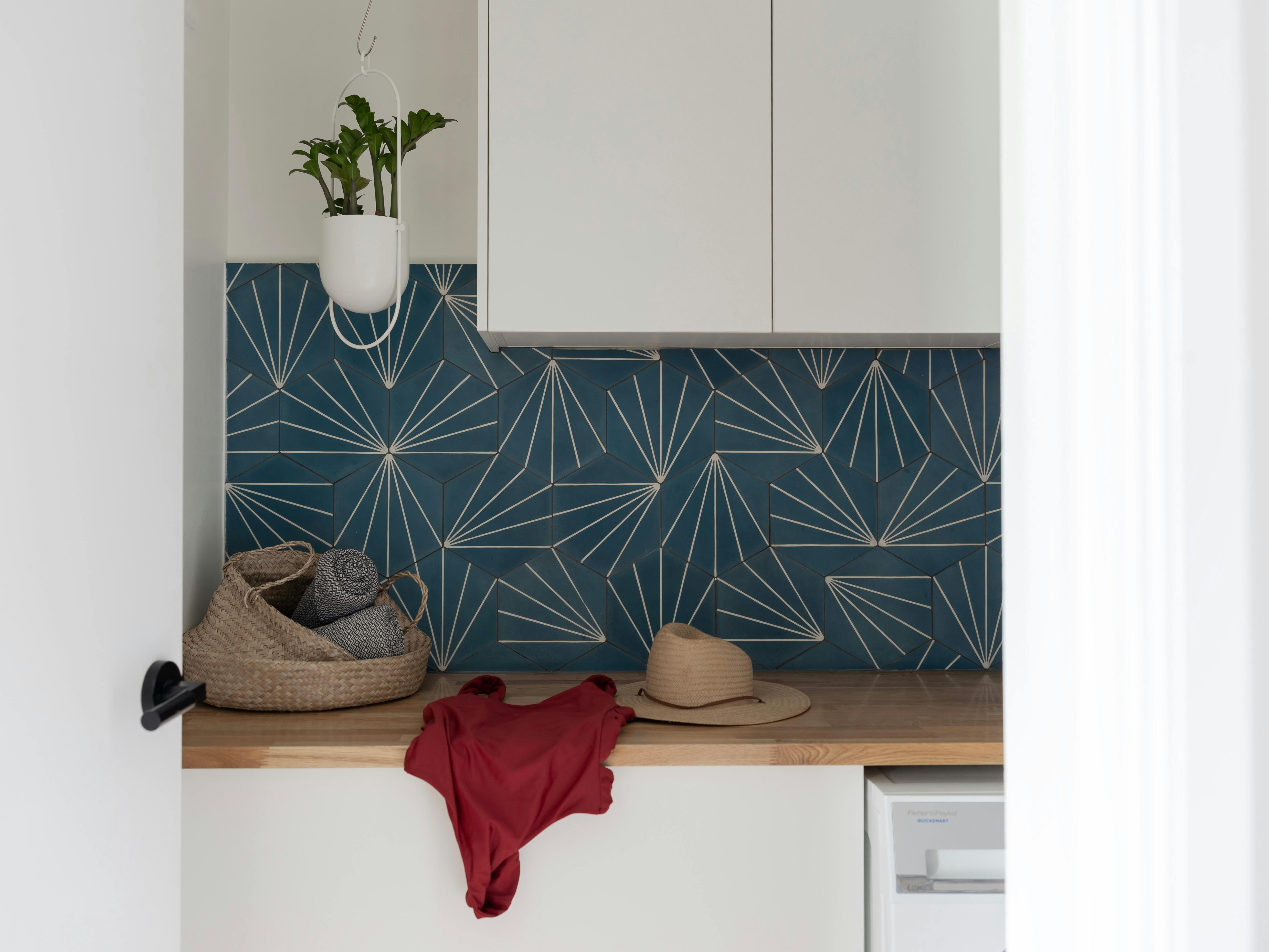 Colourful laundry, with blue and white geometric tiled wall, red swimsuit draped on timber bench top