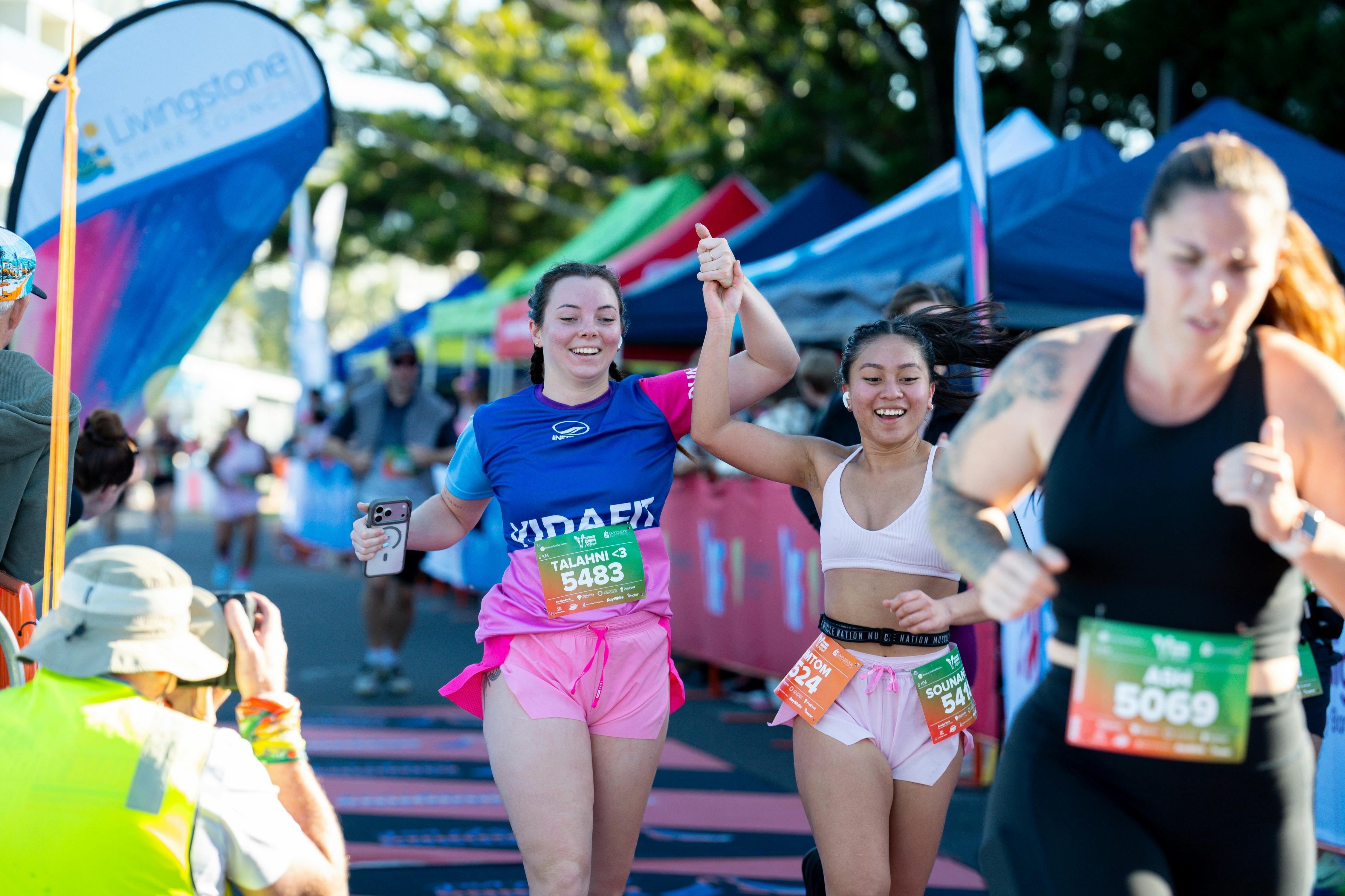 Two smiling women hold hands and celebrate as they cross the Yeppoon Running Festival finish line to