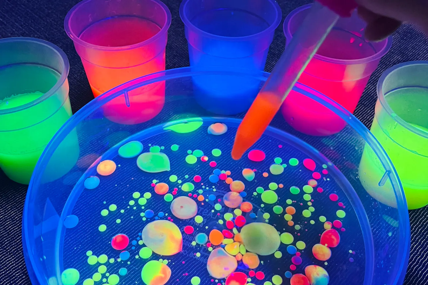 A dropper of glowing paint into oil making glowing colourful circles at Messy Glow Co UV Paint Room