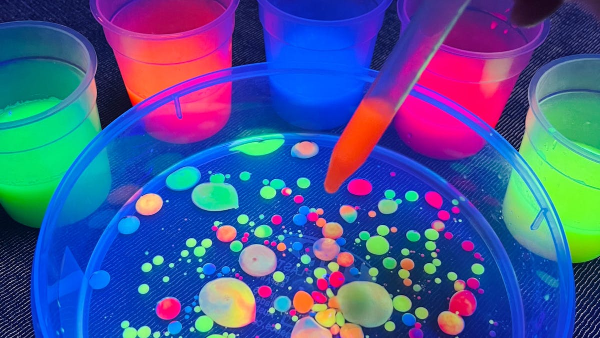 A dropper of glowing paint into oil making glowing colourful circles at Messy Glow Co UV Paint Room