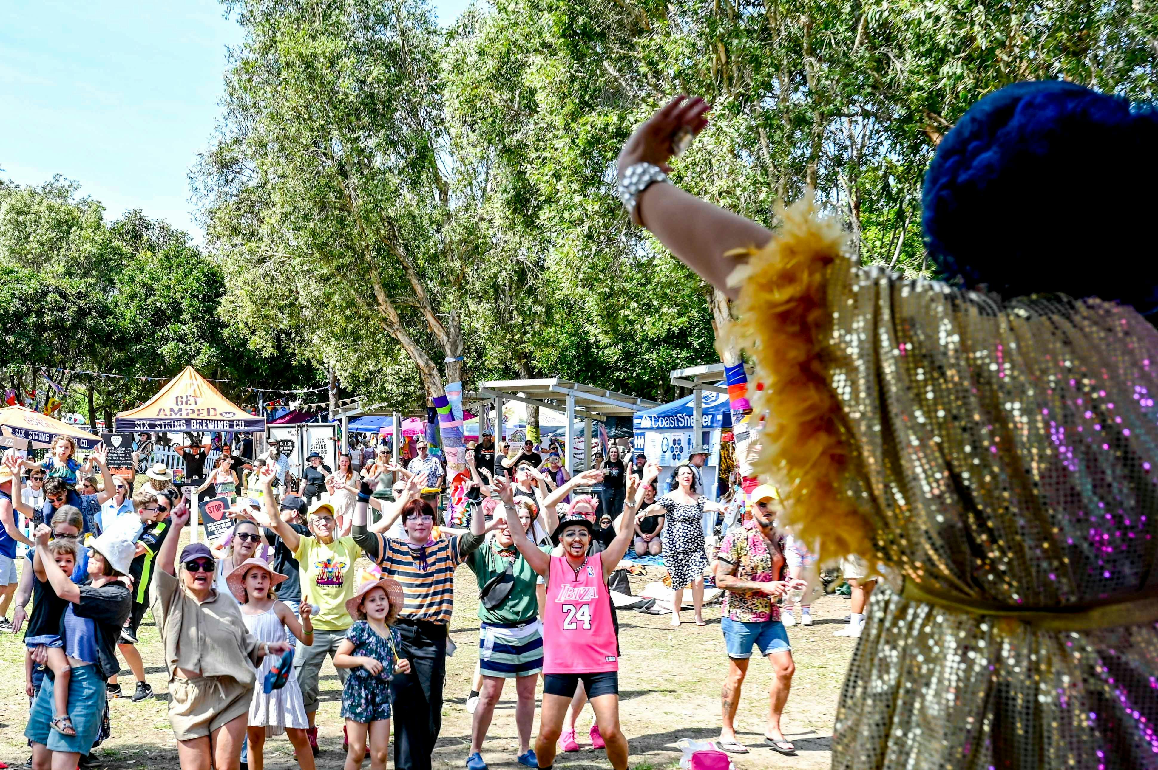 A person in a glamourous boa waving to a crowd of families with children, adults and elderly people