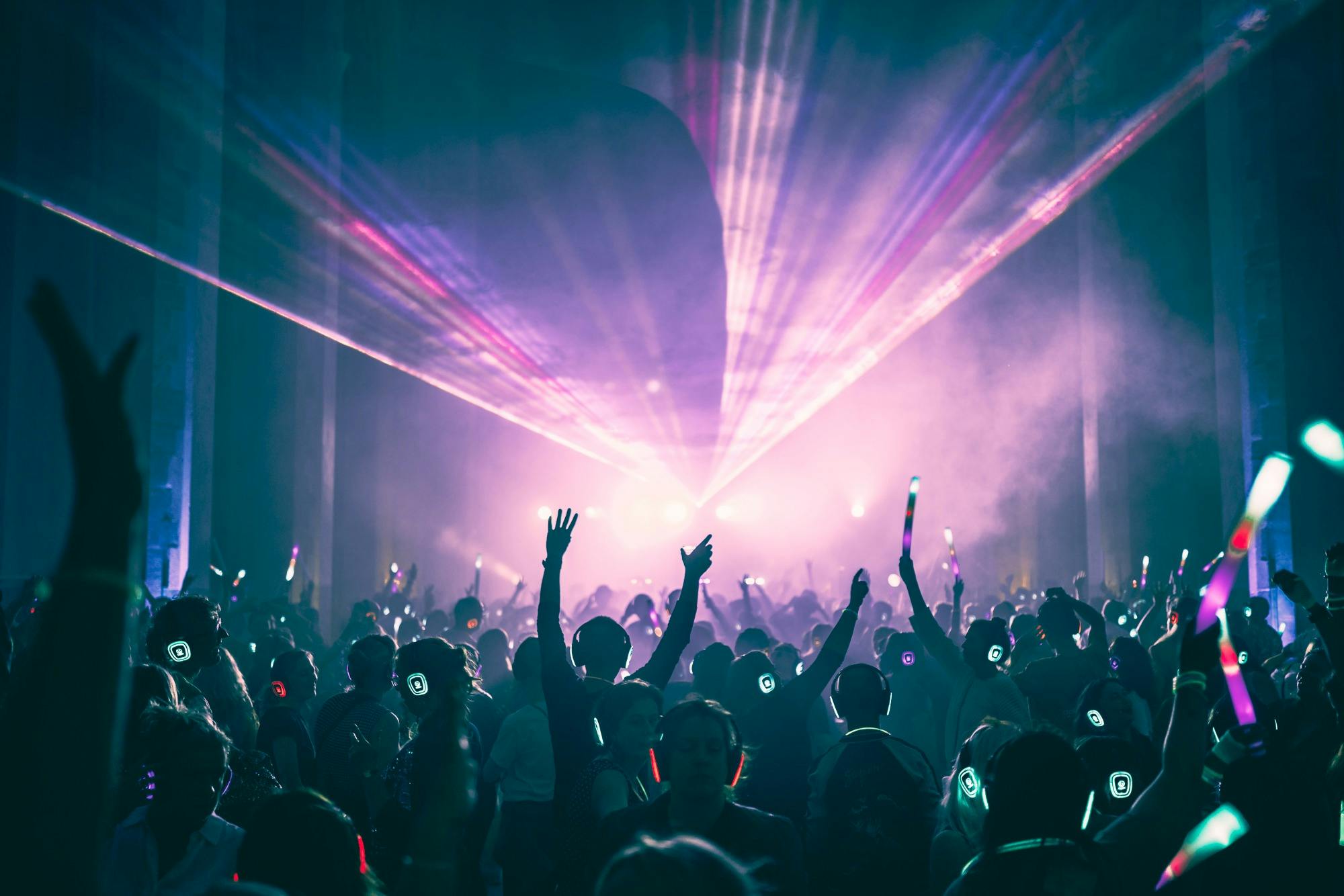 Crowd dancing to a silent disco in a hall with light show displayed above them