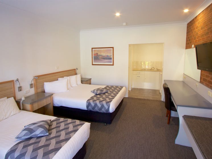Guest room with one queen bed, one single bed, kitchenette and desk with large TV.