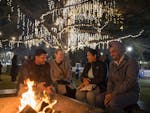 Group around firepit under fairy lights at night, smiling and enjoying the festival.