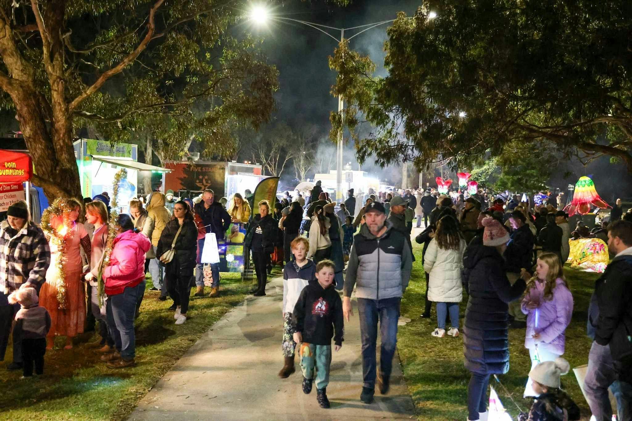 A large crowd of people gathered, with food trucks and lanterns