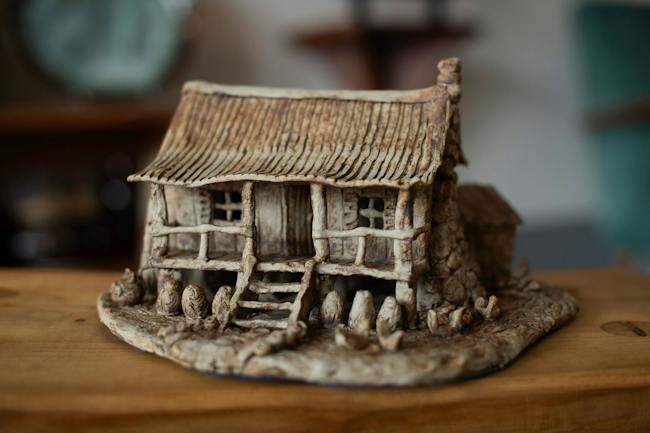 A ceramic sculpture of a traditional stilt house with a textured, ridged thatch-style roof.