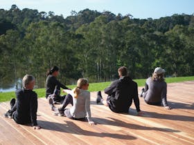 People doing yoga on a timber deck with views of lake and bushland