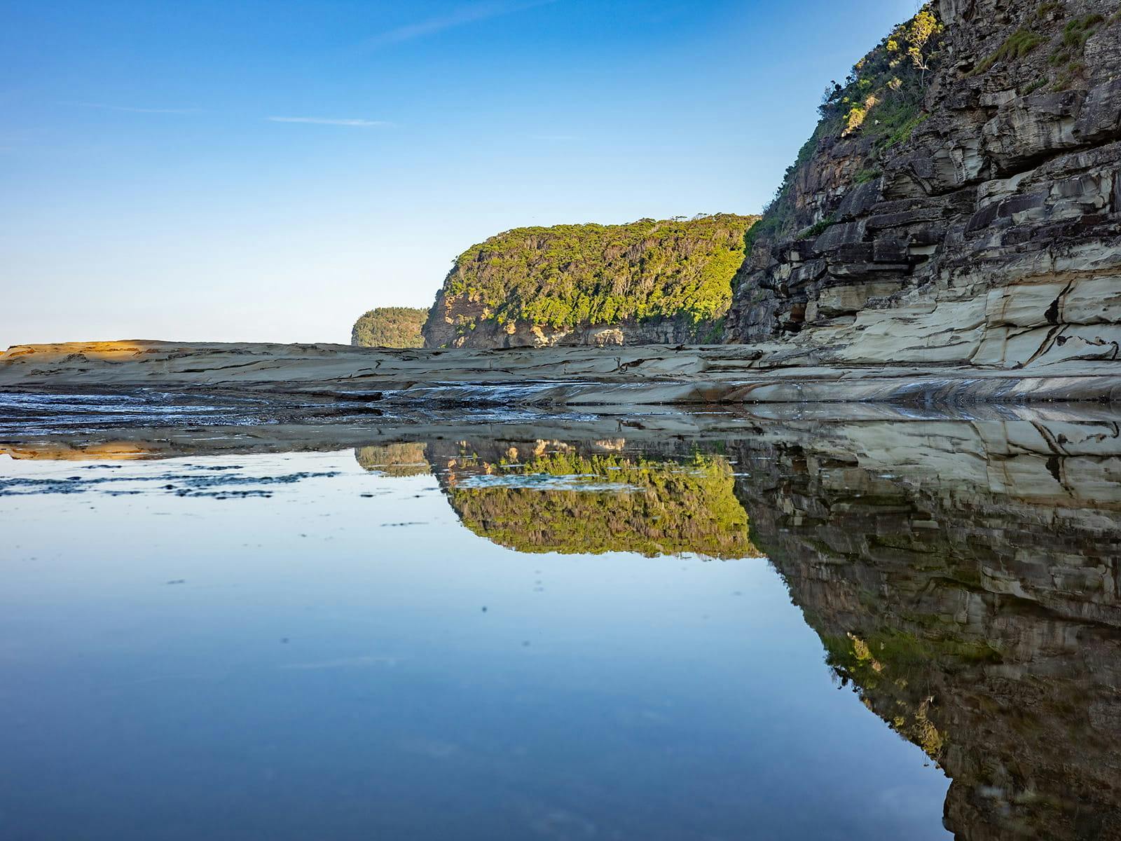 Rocky coastal cliffs reflected in calm tidal pools on a sunny day near Sydney.