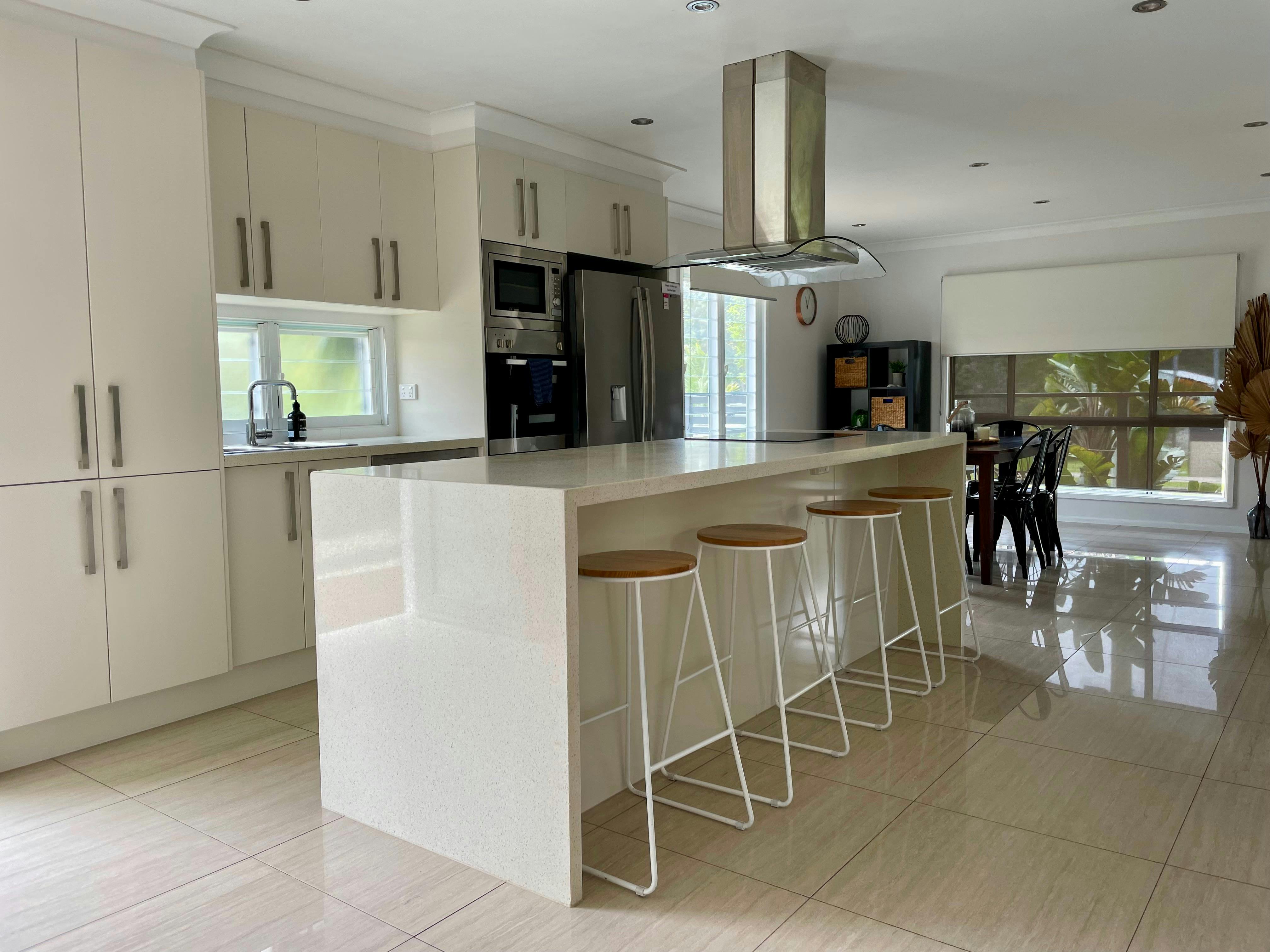 4개의 바 의자와 타일 바닥을 갖춘 현대식 주방. 주방에는 싱크대와 창문이 있습니다.