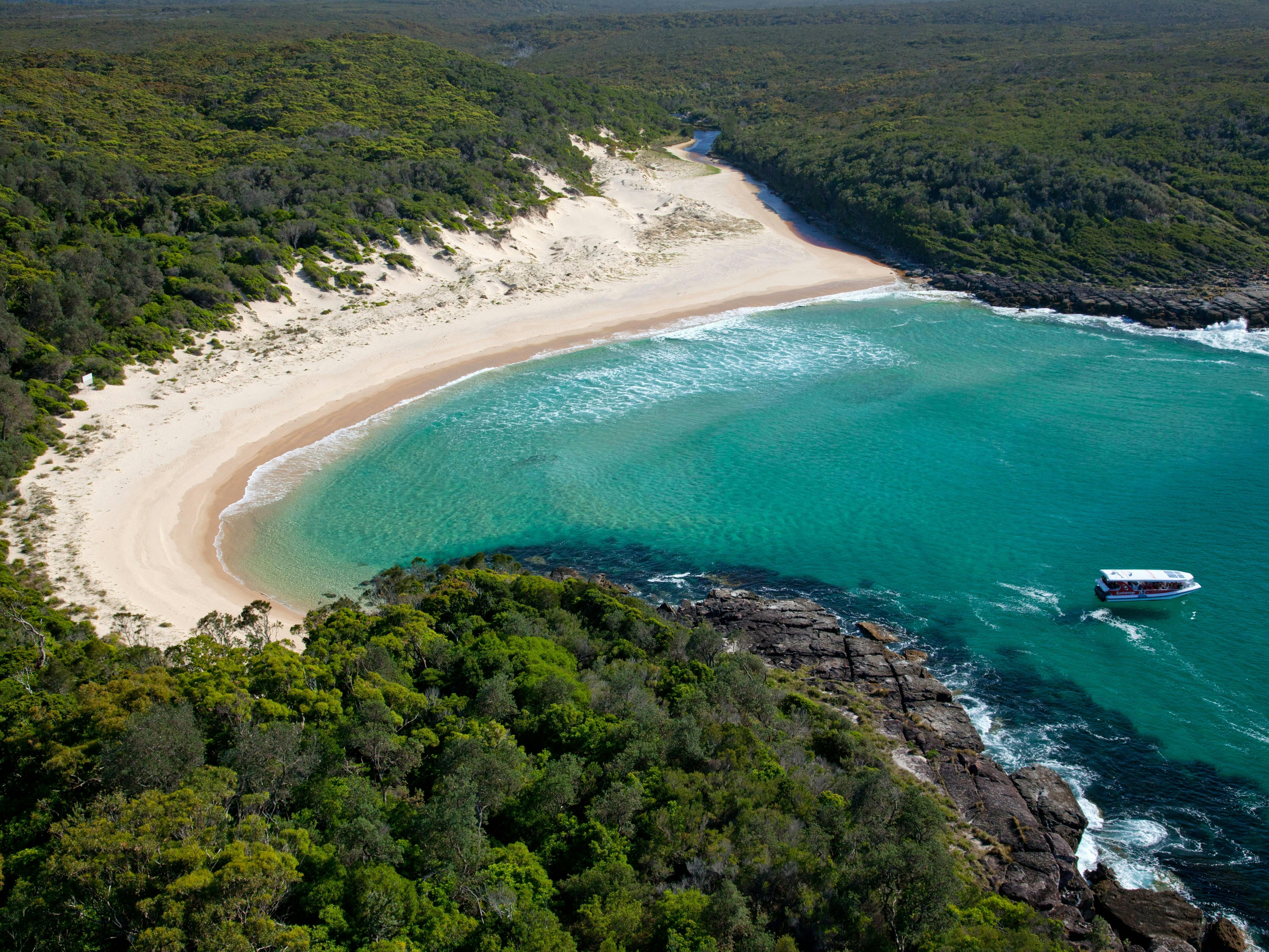 Boat in turquoise bay with white sand and bushland