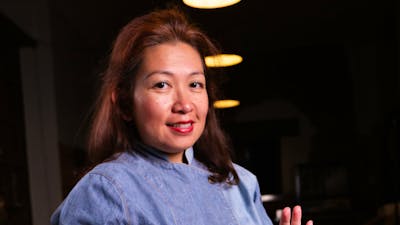 Chef Daniar warm evening lights, denim chef attire, holding gule domba (lamb gule) in a black bowl..