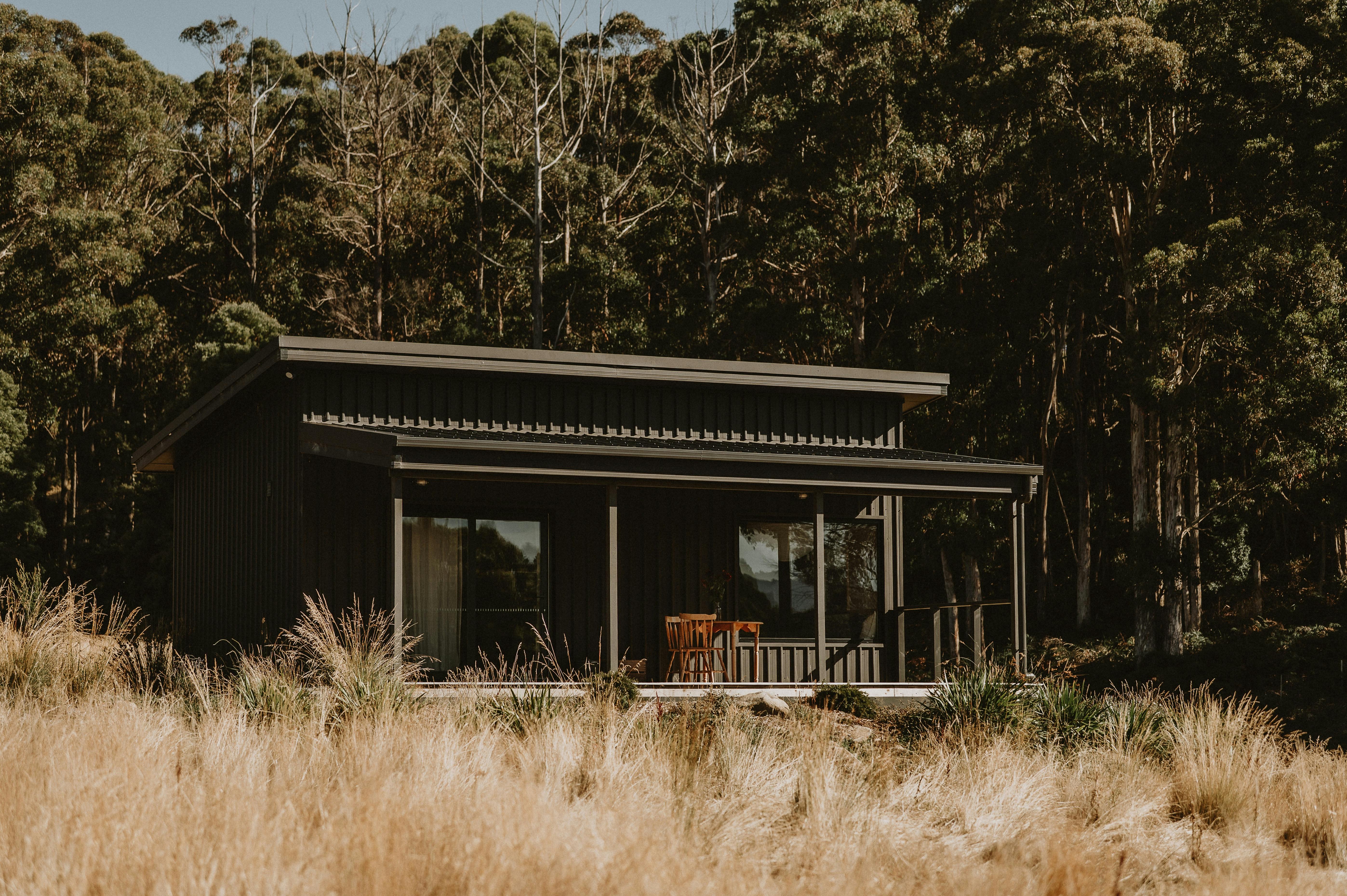Dark grey cabin with a deck and trees behind.