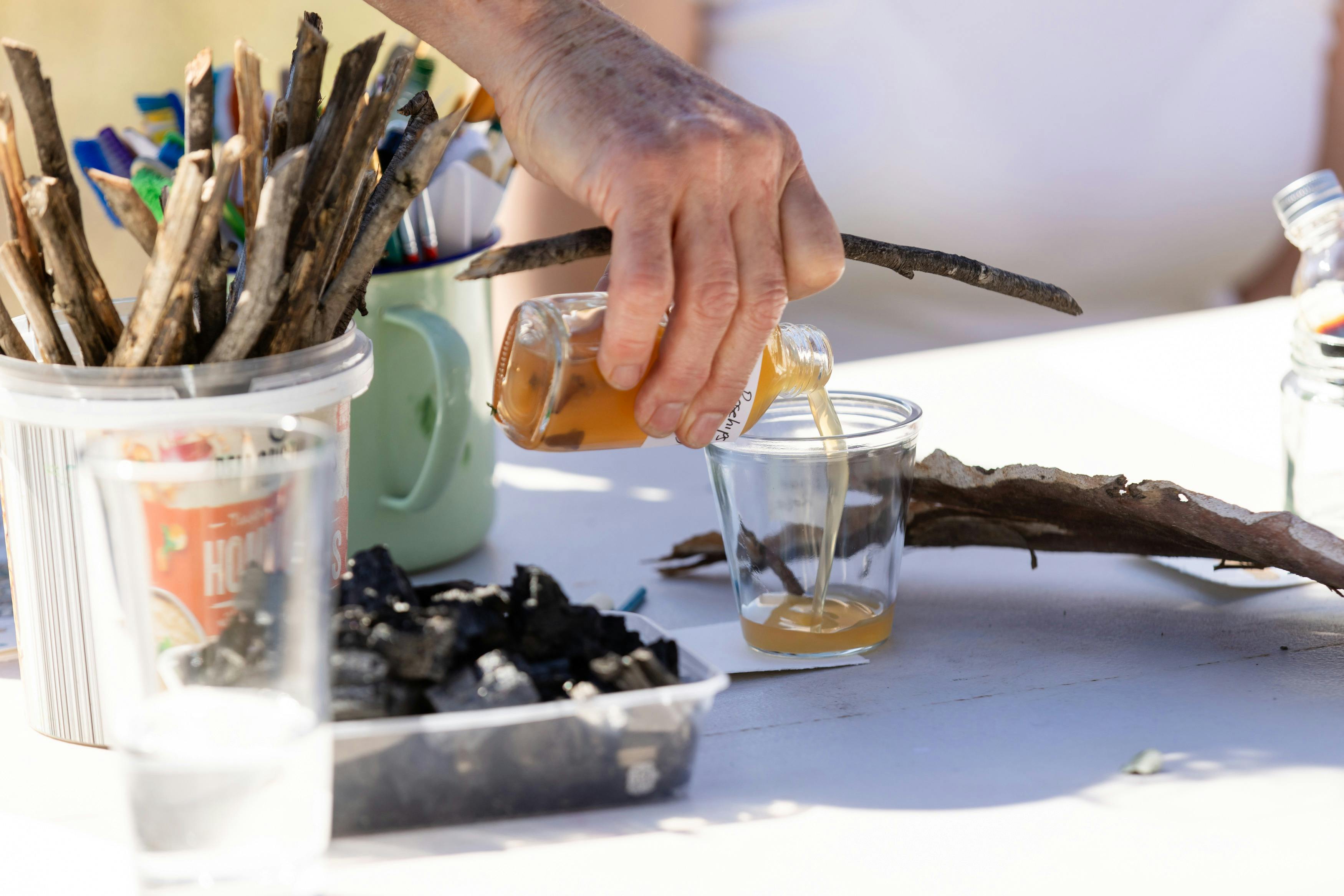 Art supplies on a table. Someone is pouring liquid into a cup on the table.