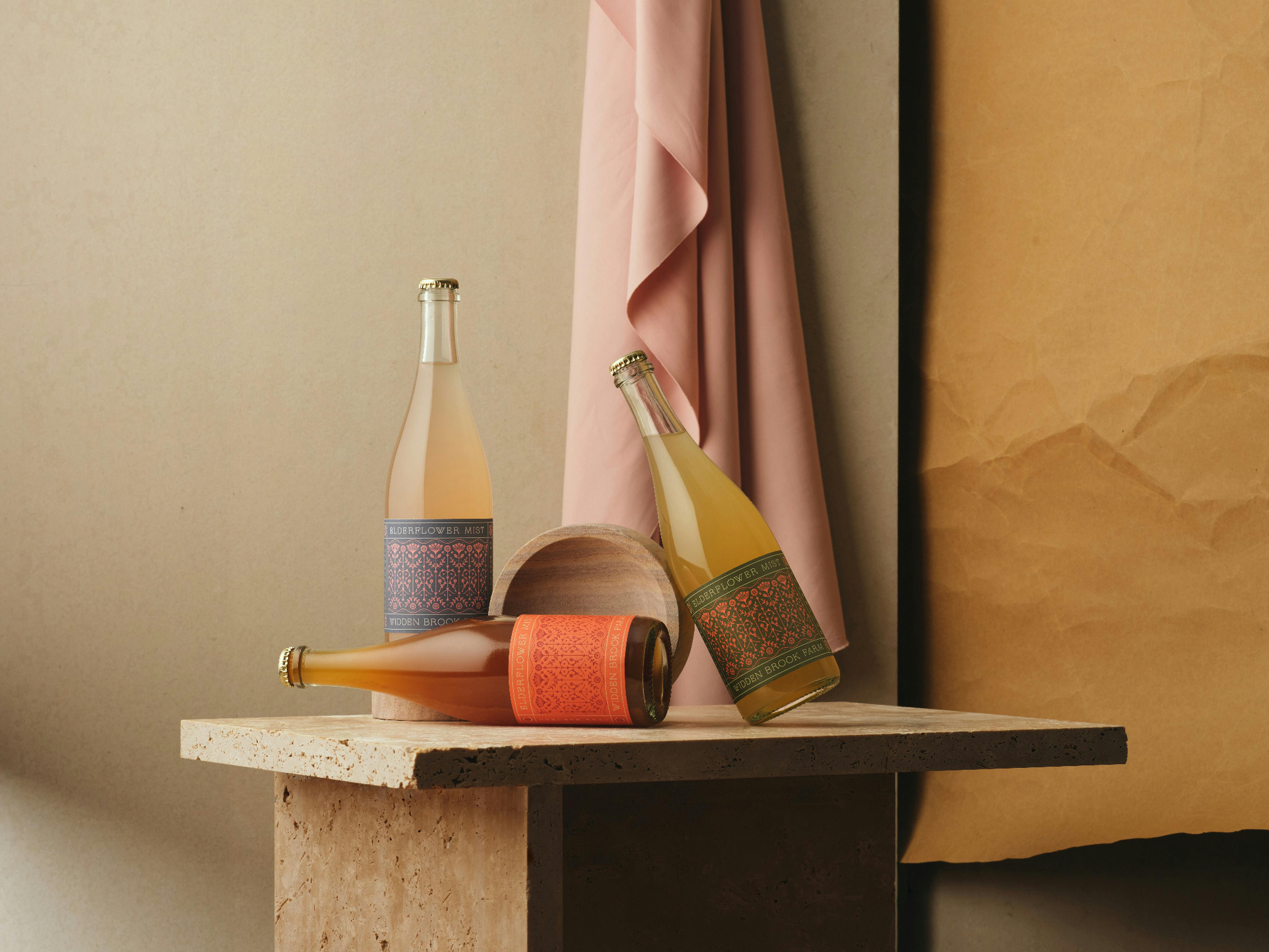Three bottles of Elderflower Mist Sparkling resting on a stone plinth against a warm backdrop