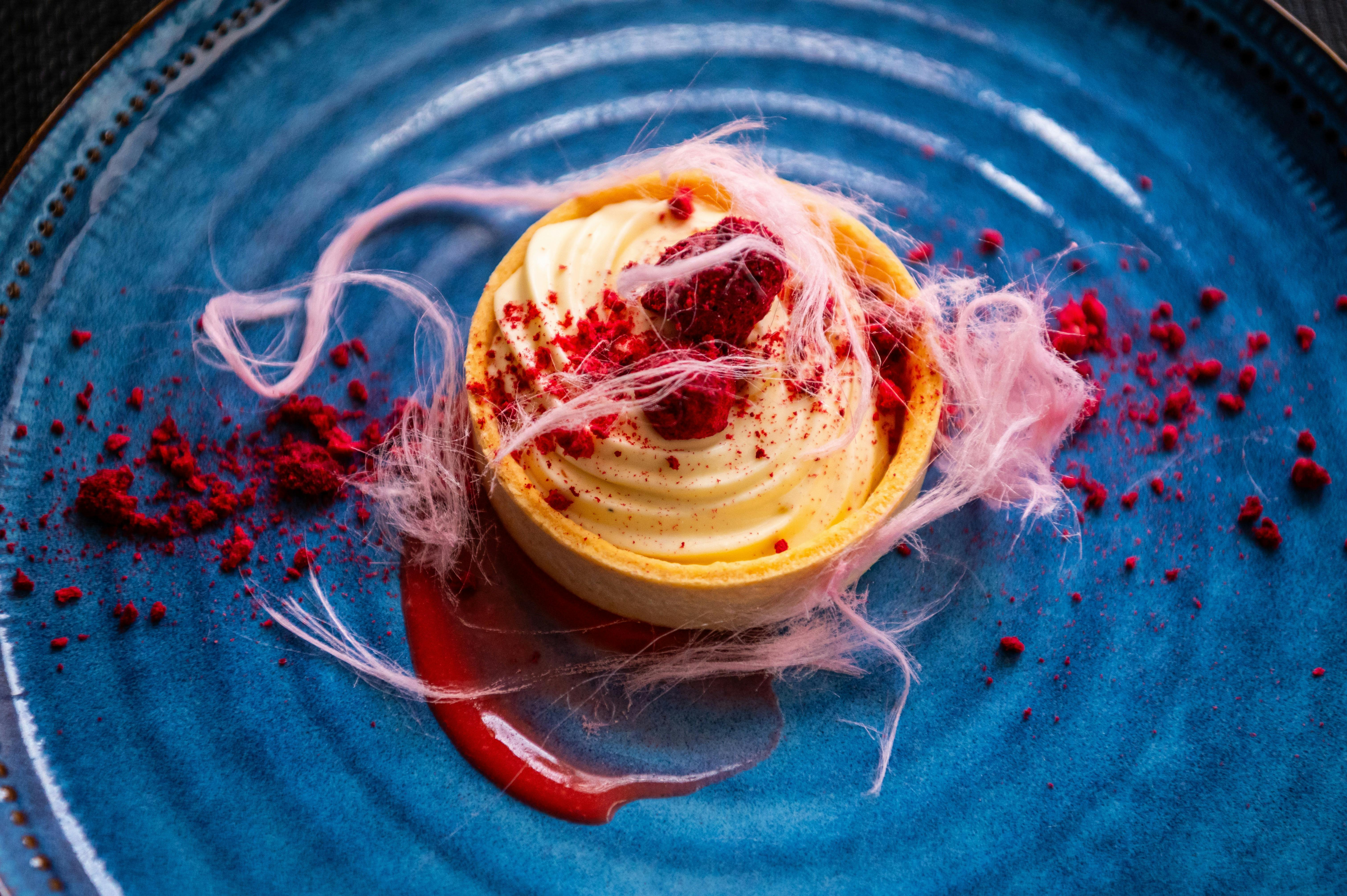 Cheesecake tart with raspberry and pink fairy floss on blue plate