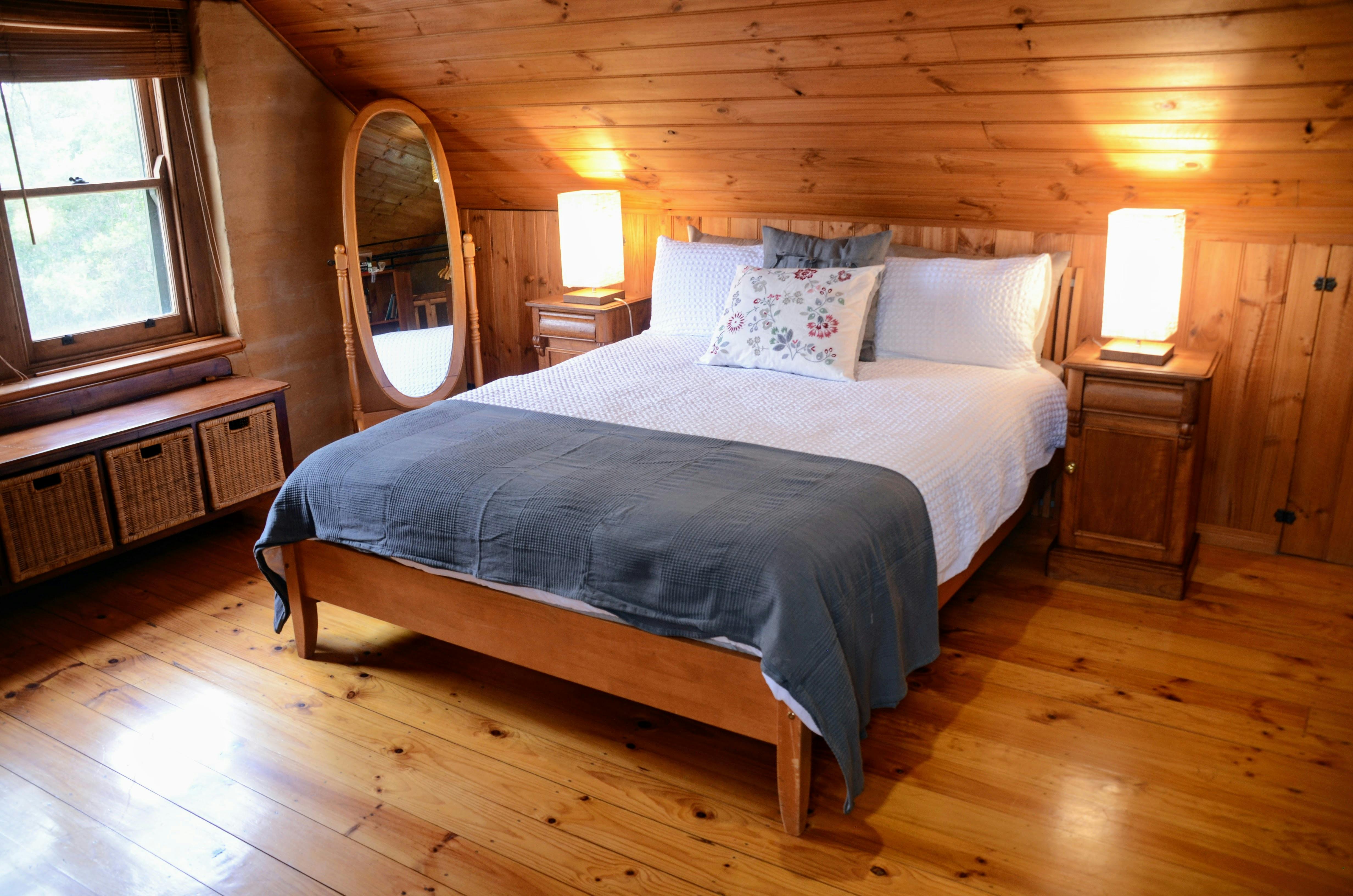 A wooden queen bed with white bedding and a grey woolen blanket