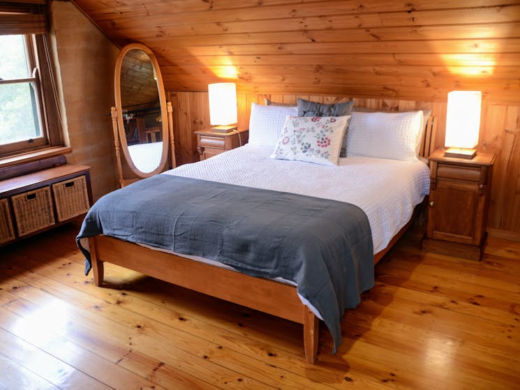 A wooden queen bed with white bedding and a grey woolen blanket