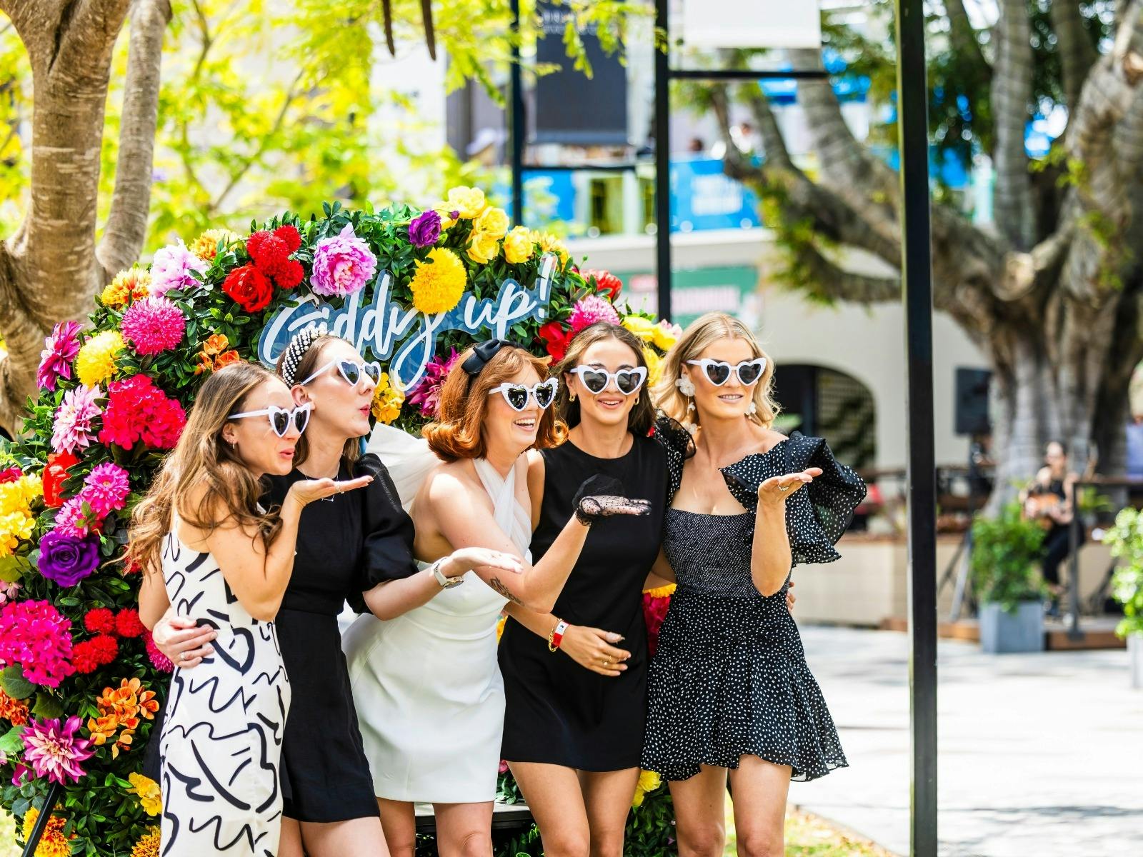Racegoers pose in front of a Spring Racing Carnival floral wreath
