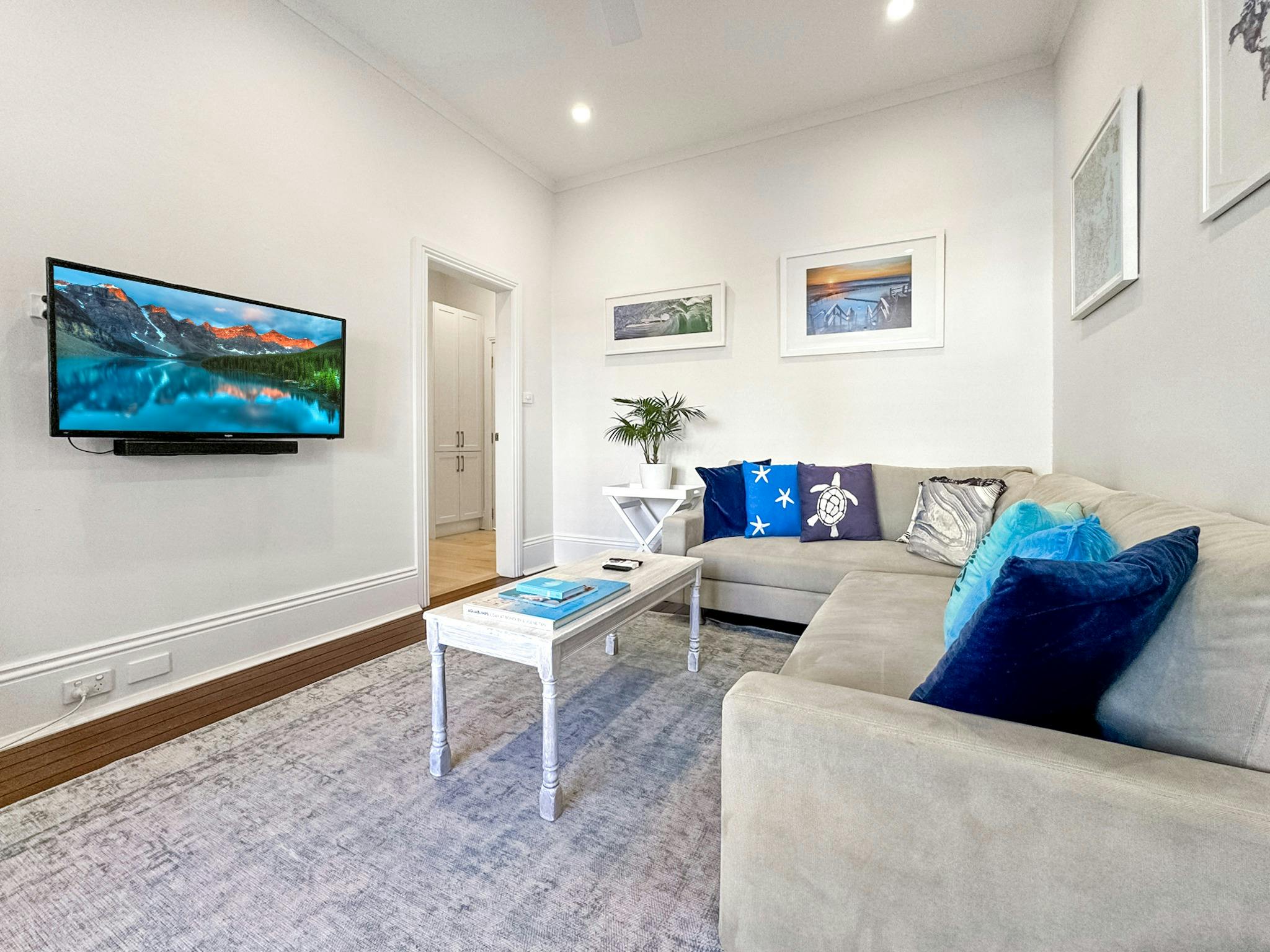 客廳的牆上配有電視、中性色調的沙發和海灘主題的藝術品。