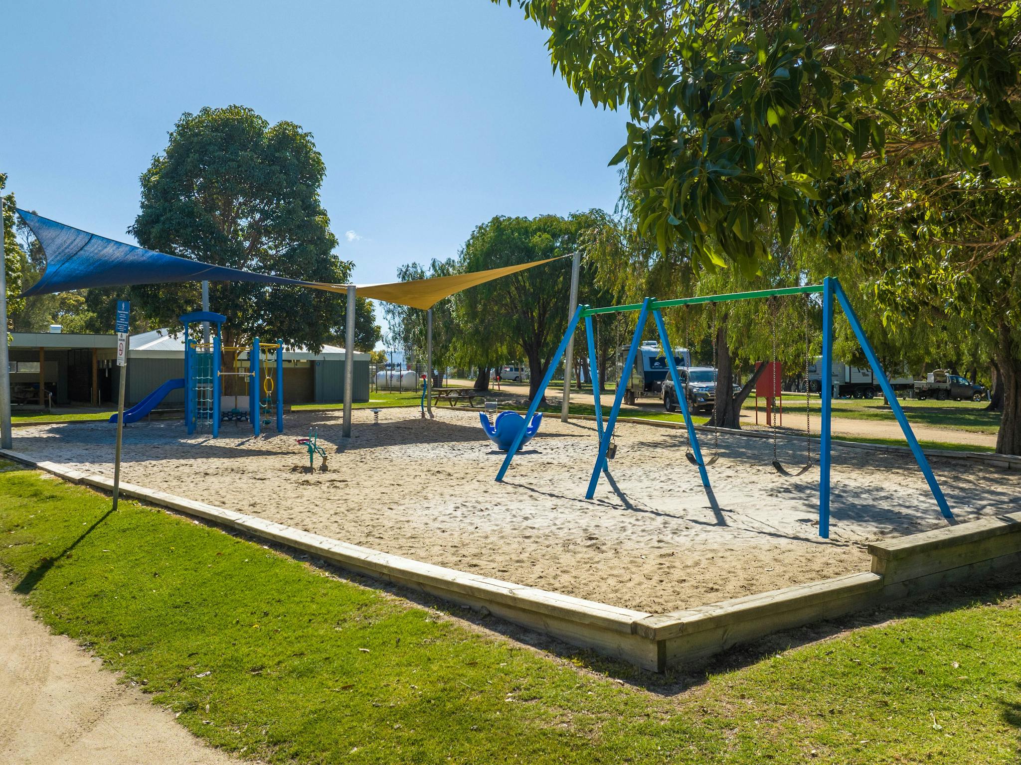 Playground with shade sails and sandy flooring surrounded by trees