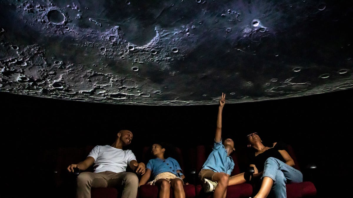 Family seated in a Planetarium theatre looking up at a Moon image