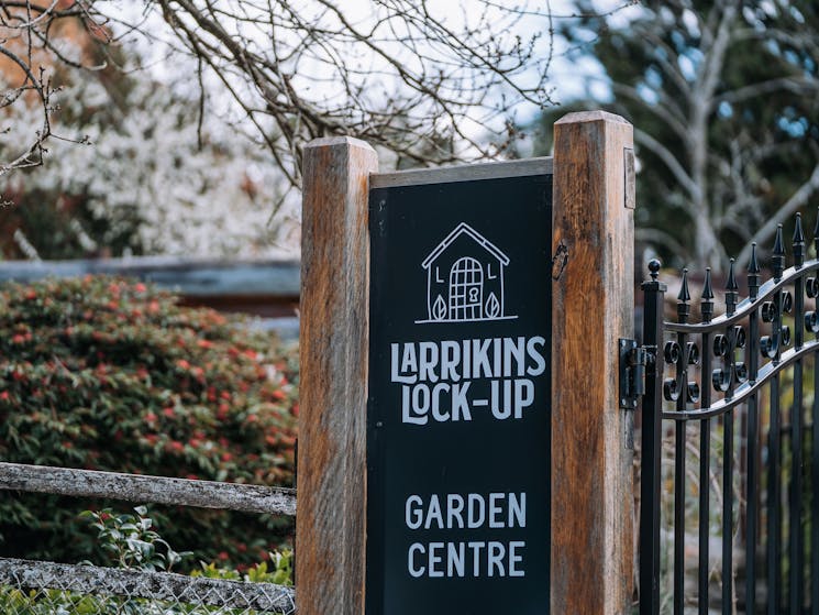 Timber and printed signage for Larrikins Lockup stands either side of a feature iron gate