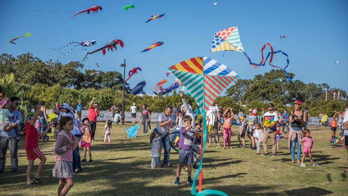 Children running around on a grass area flying kites