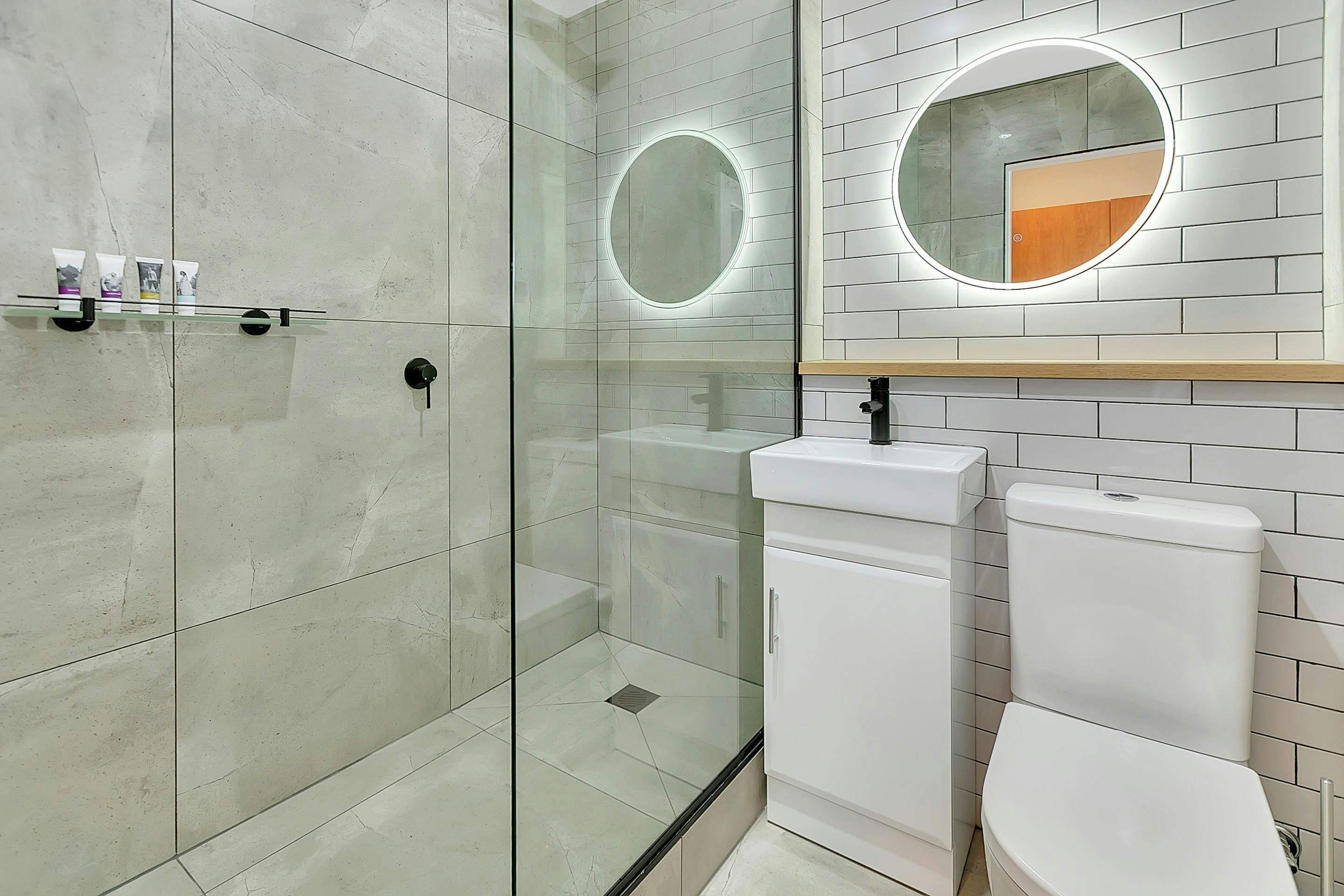 Contemporary bathroom, white, showing shower, toilet, hand basin and mirror.