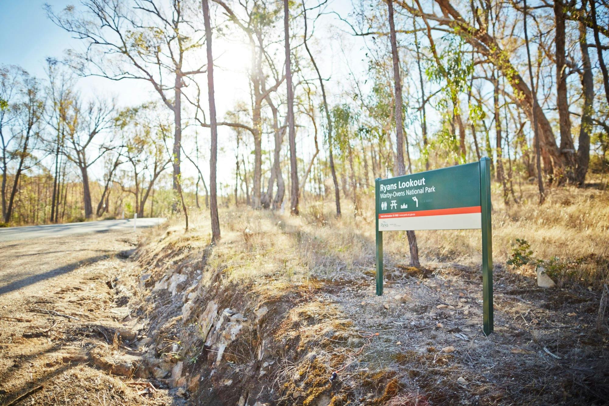 Ryans Lookout sign, showing toilet, picnic, fire lookout symbols, trees, sunlight, rocky drain, road