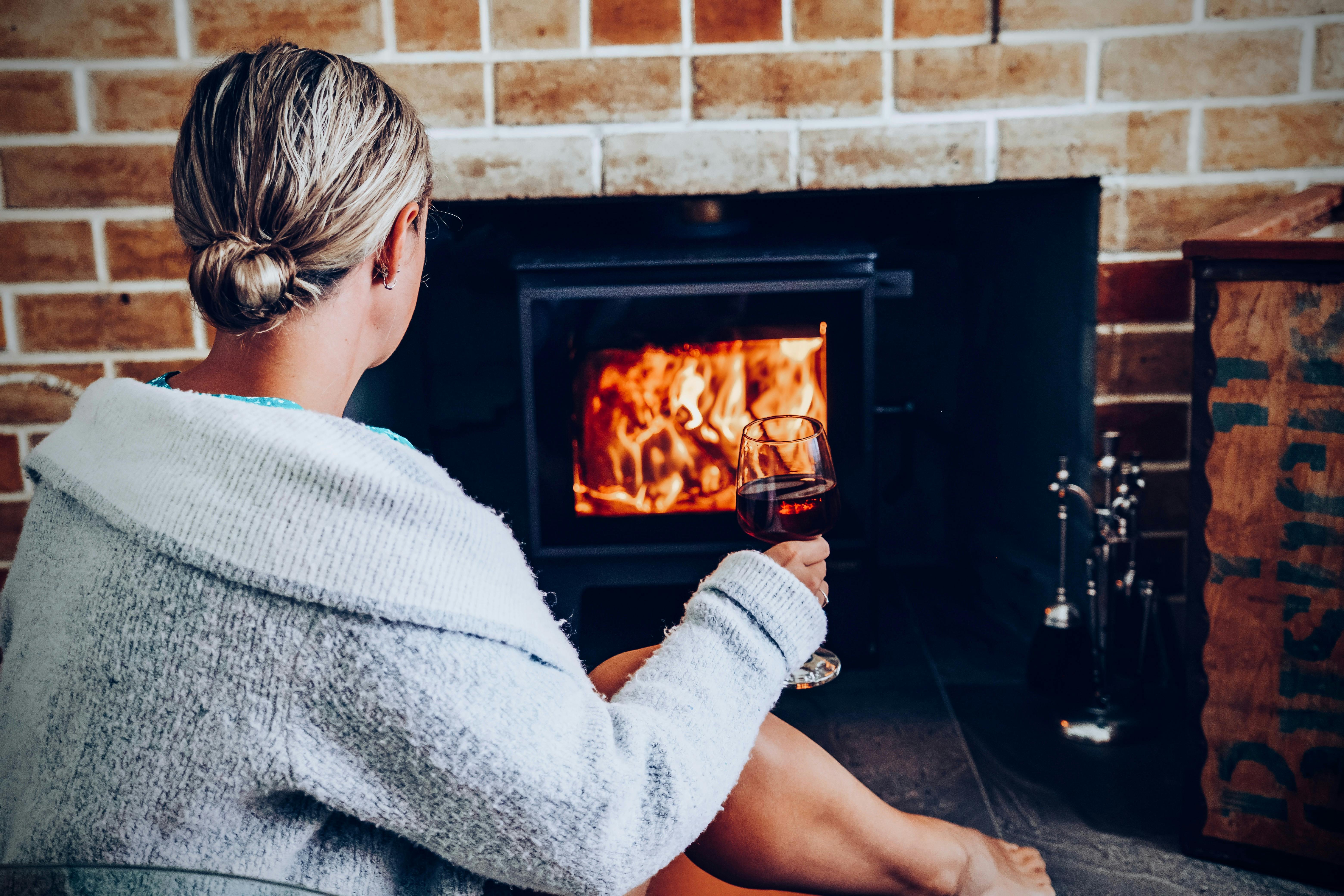 Wood burning fireplace, woman relaxes by fire with a glass of wine.