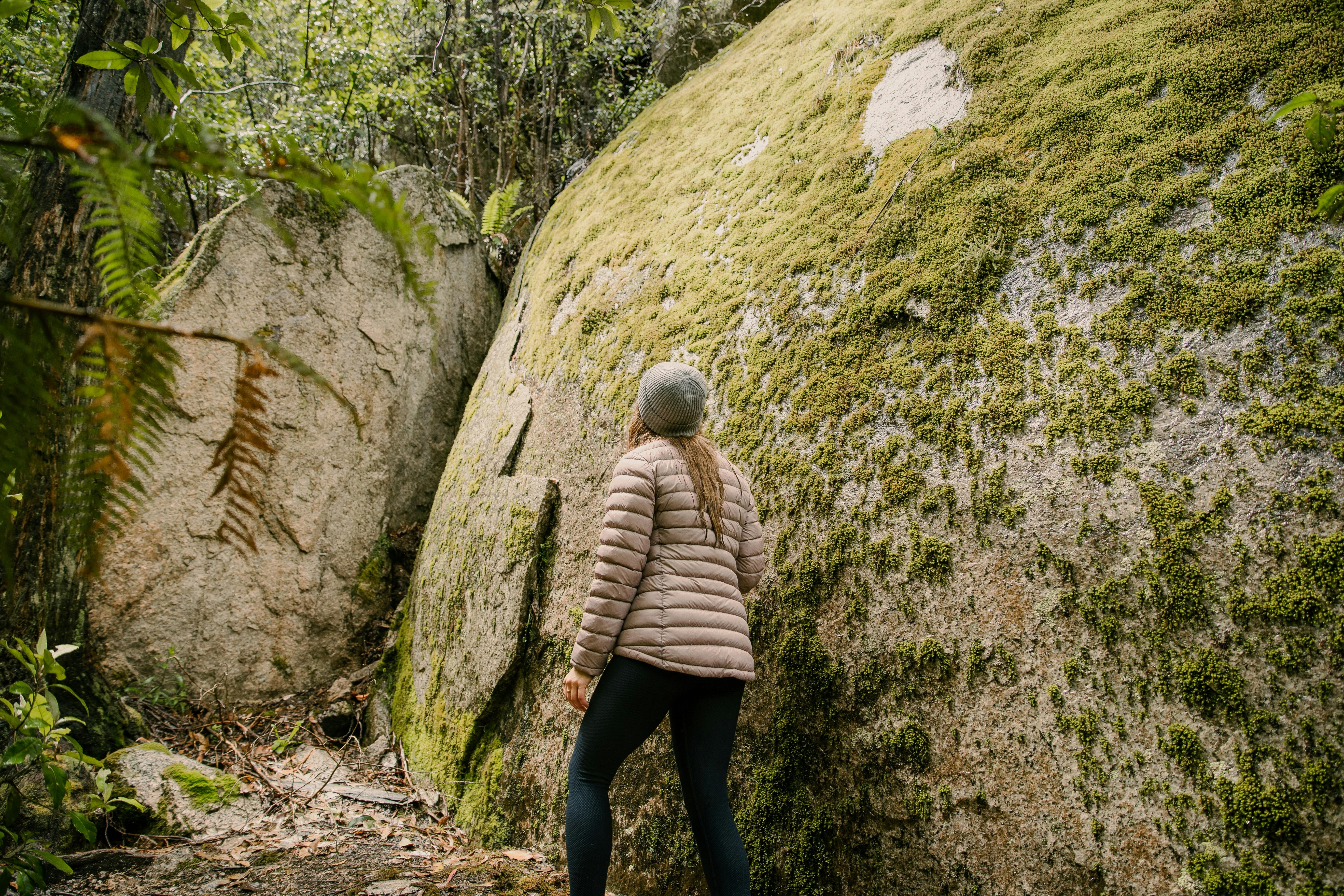 Woman hiking beside huge moss covered granite boulder