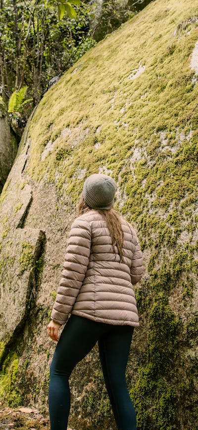 Woman hiking beside huge moss covered granite boulder