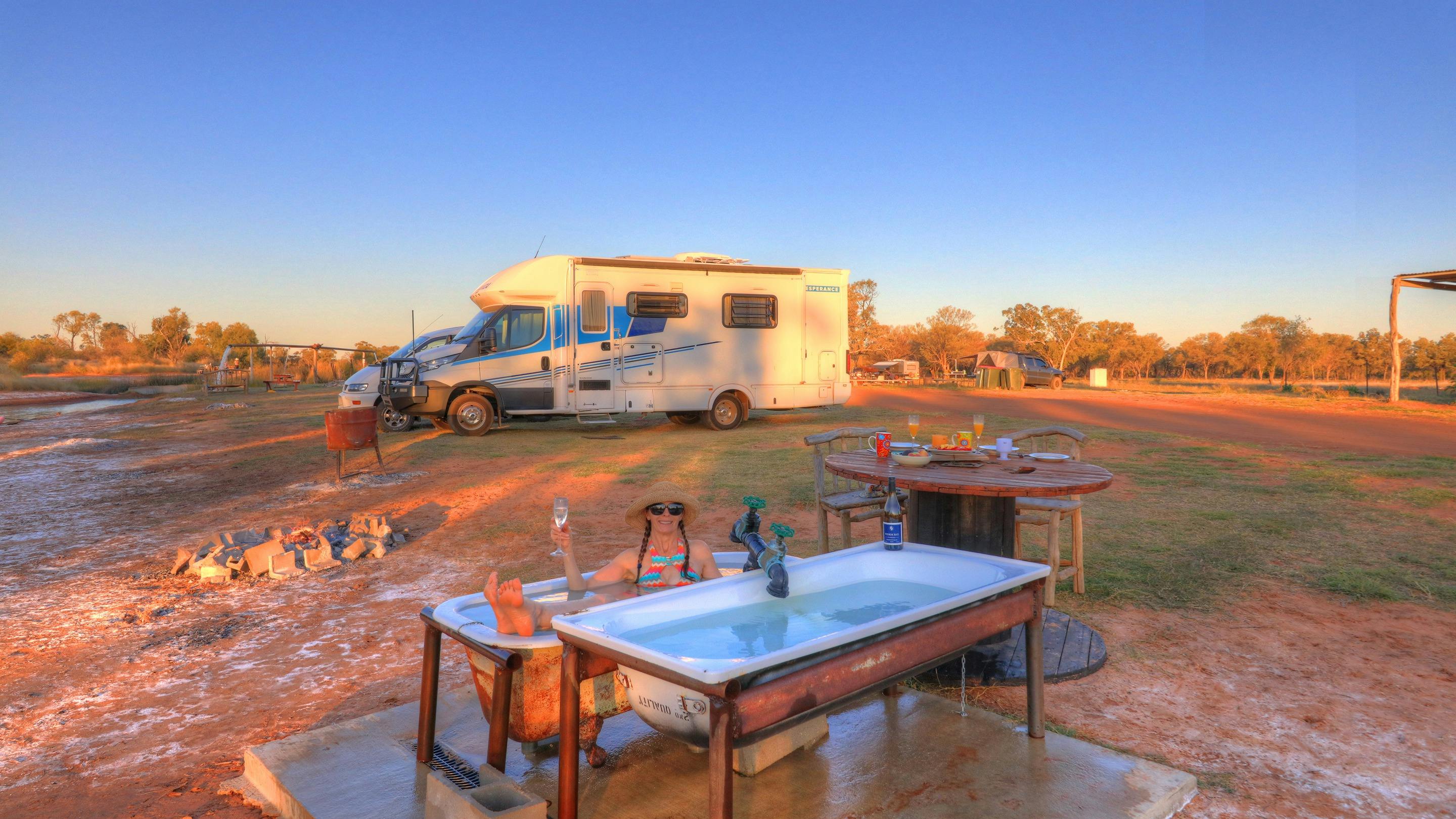 A woman in a hot outdoor bath with caravan behind at the Bore Campsite, Charlotte Plains