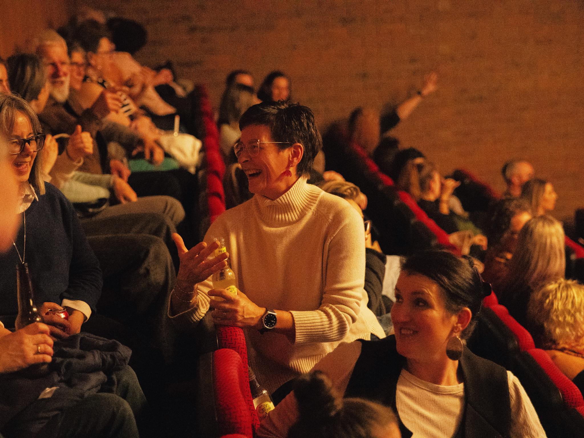 Two audience members are turning around in their seat to talk to the audience sat directly behind