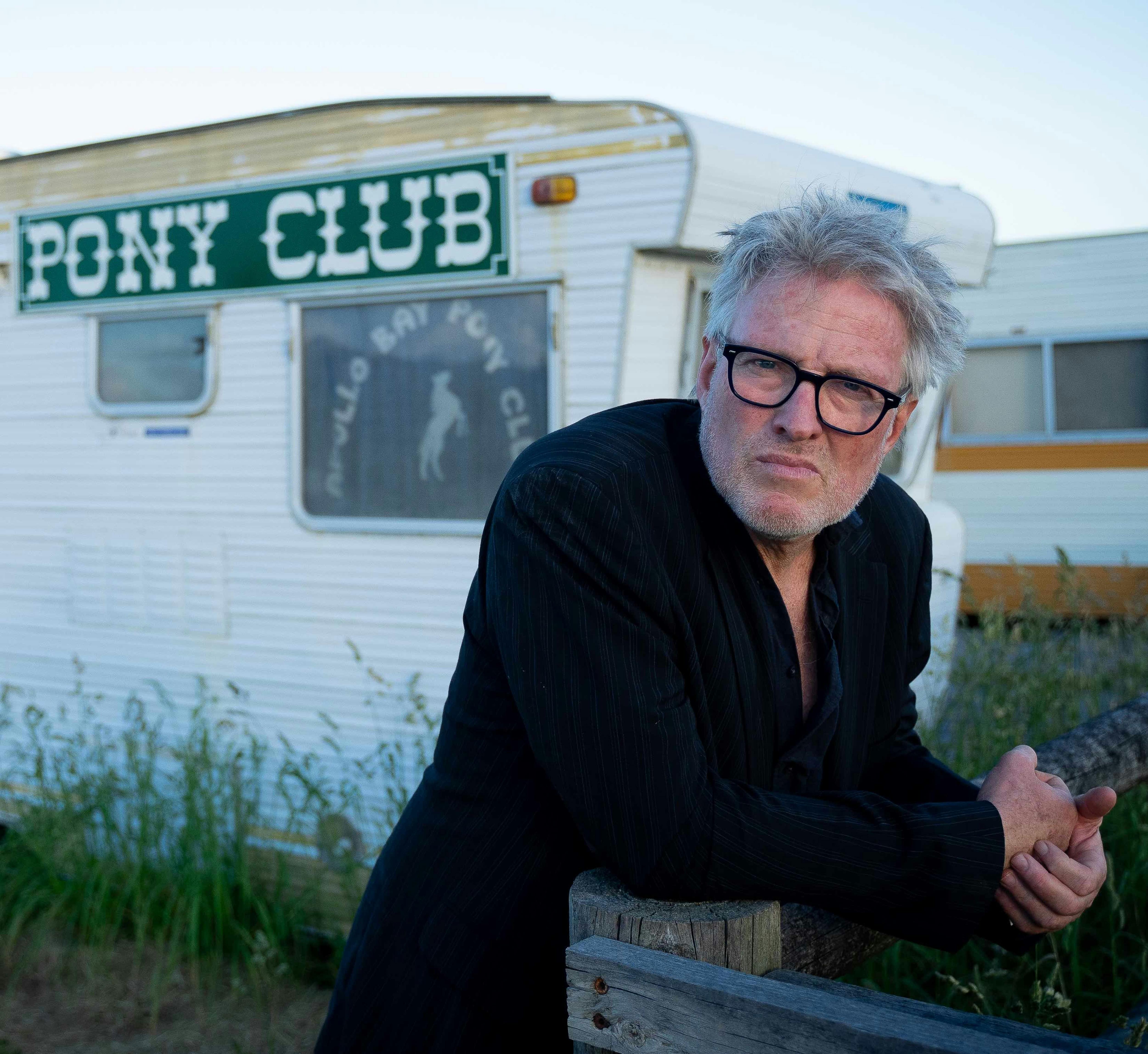 man leaning on something outside with a caravan in the background
