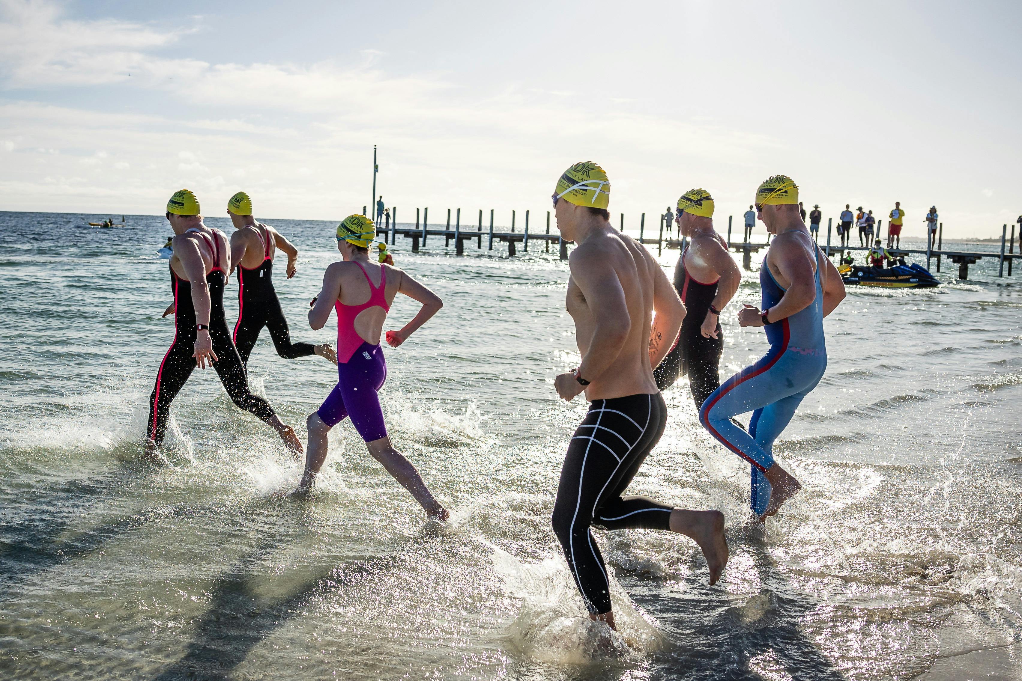 Several swimmers running into the water at the start line.