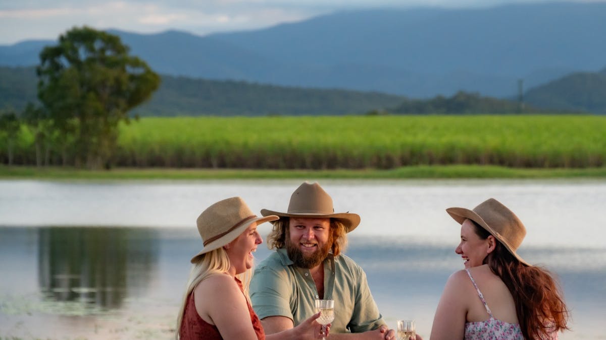 Three people enjoying a drink with the Oh Deere farm dam in the background