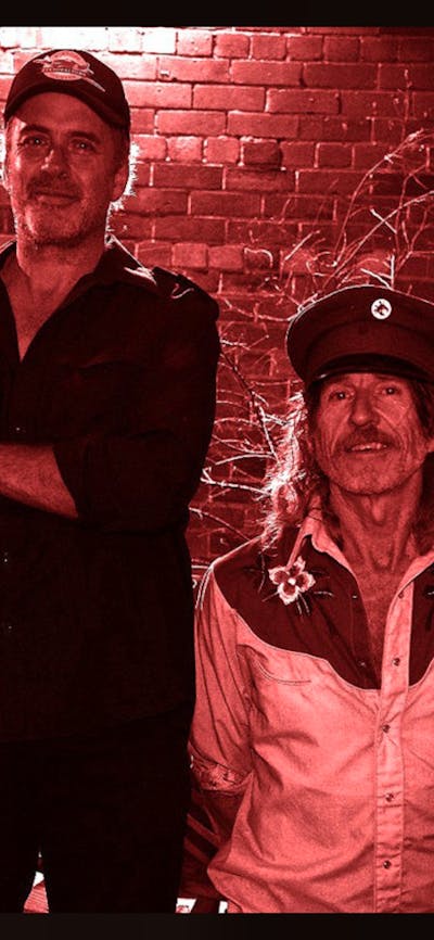 A photo of two men standing next to each other in front of a brick wall