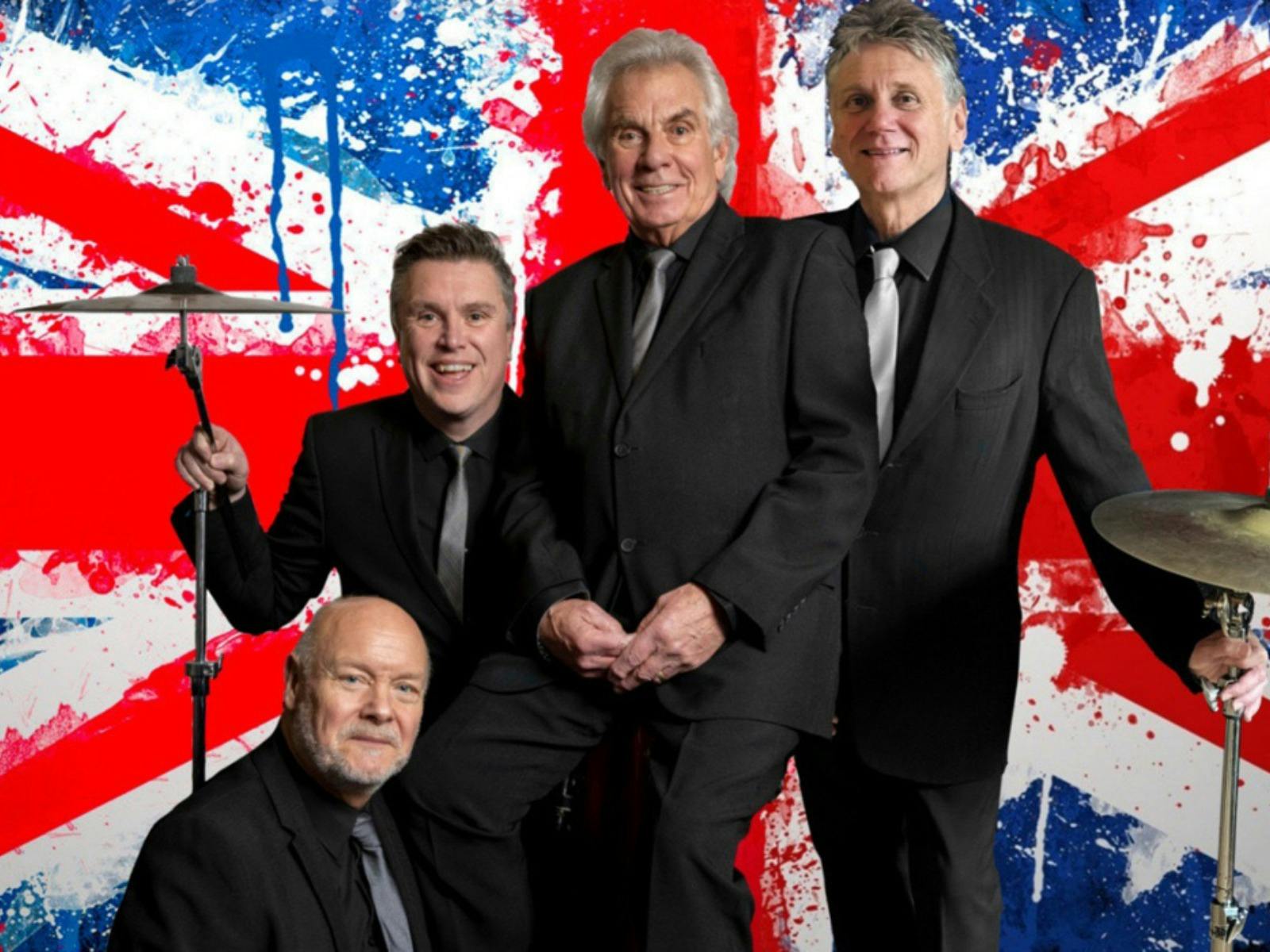 Four men in black suits pose with musical instruments, in front of a large, painted British flag