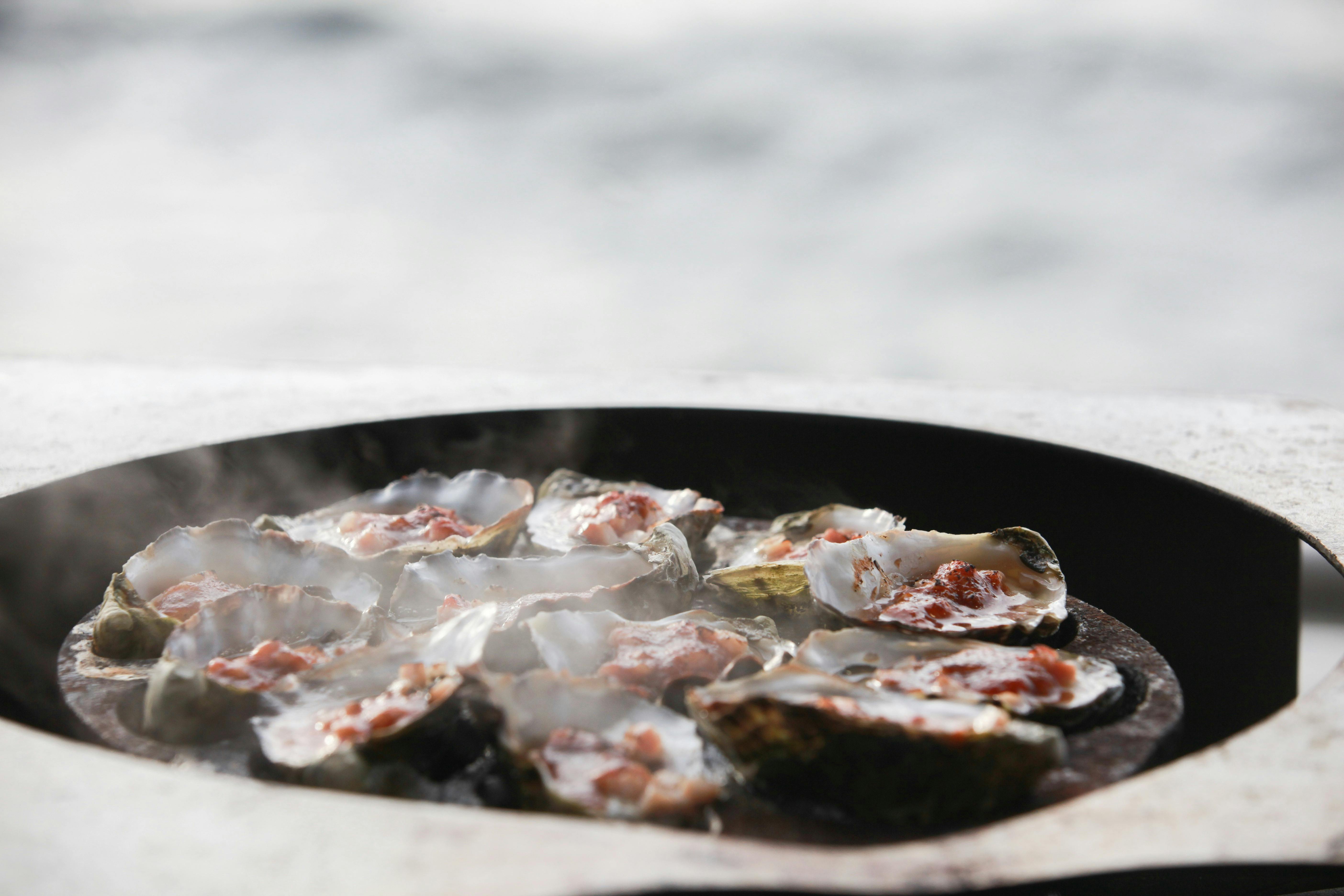 Steam coming from kilpatrick oysters as they are being cooked with the water in the backgroundound