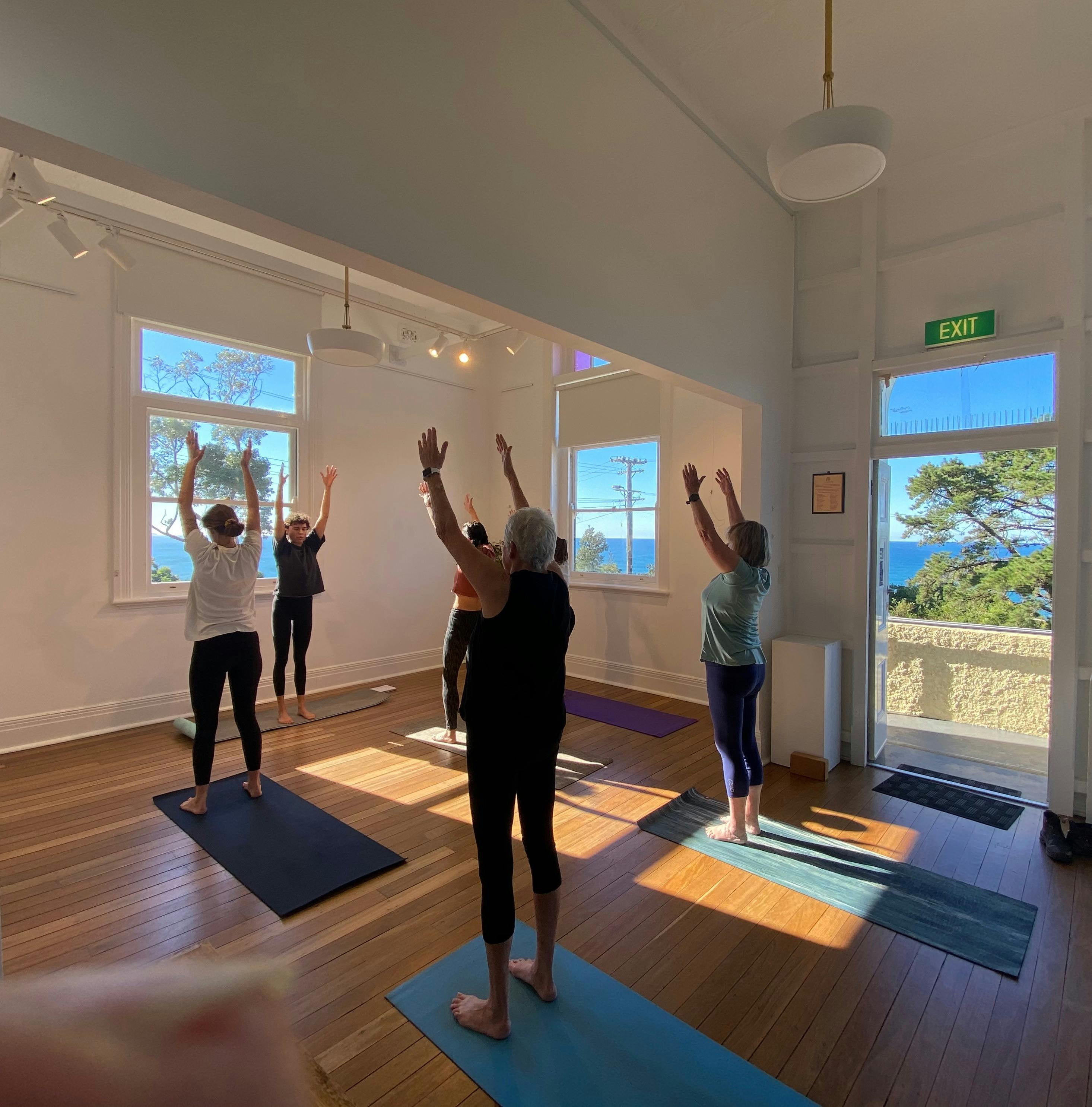 日当たりの良い部屋でヨガを練習している女性のグループ。窓越しに海が見えます。