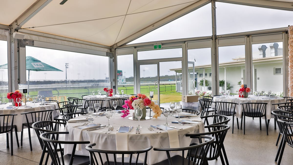 Large round tables set for dining with floral centre pieces in a large marquee
