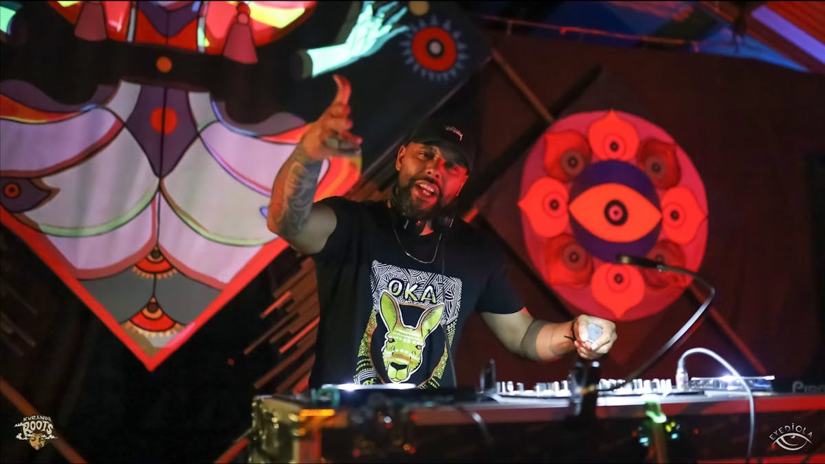 A DJ performs at Kuranda Roots Festival near Mareeba FNQ, fluorescent art surrounds him.